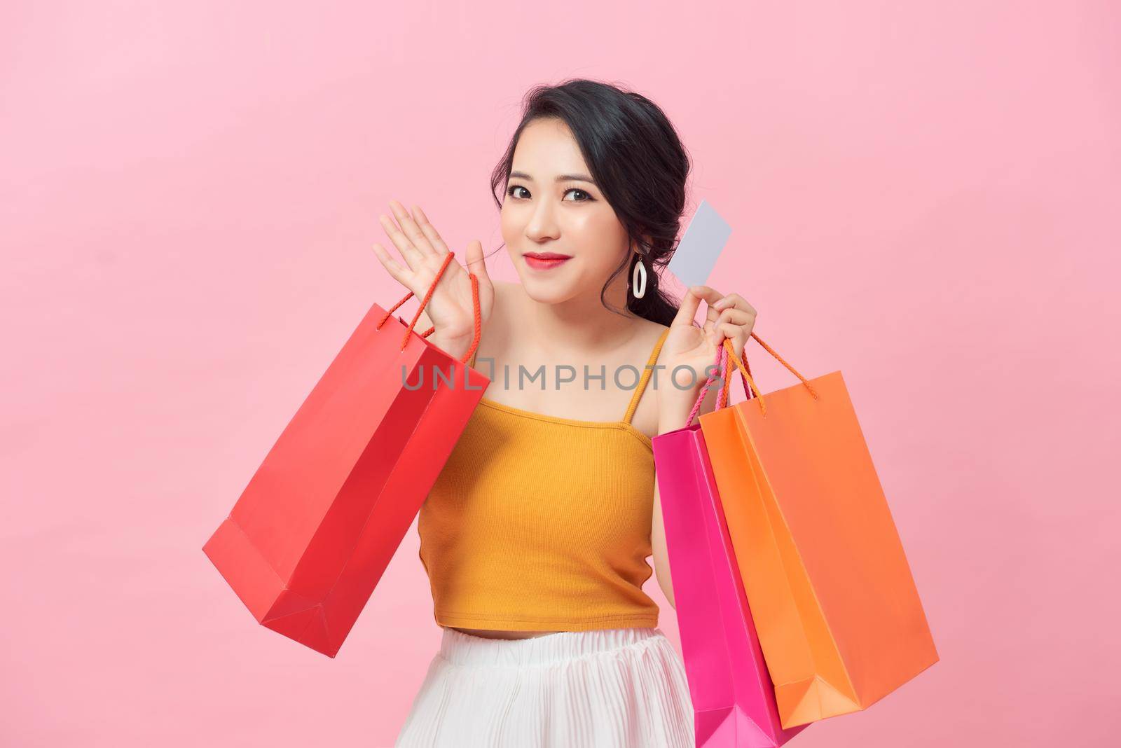 Close-up portrait of happy young Asian woman holding credit card and colorful shopping bags, isolated on pink background by makidotvn