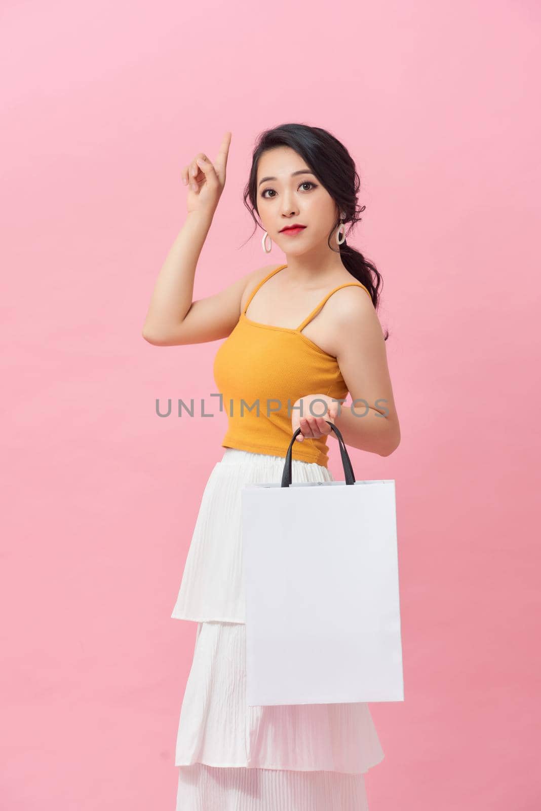 Beautiful Asian woman holding shopping bag while over pink background.