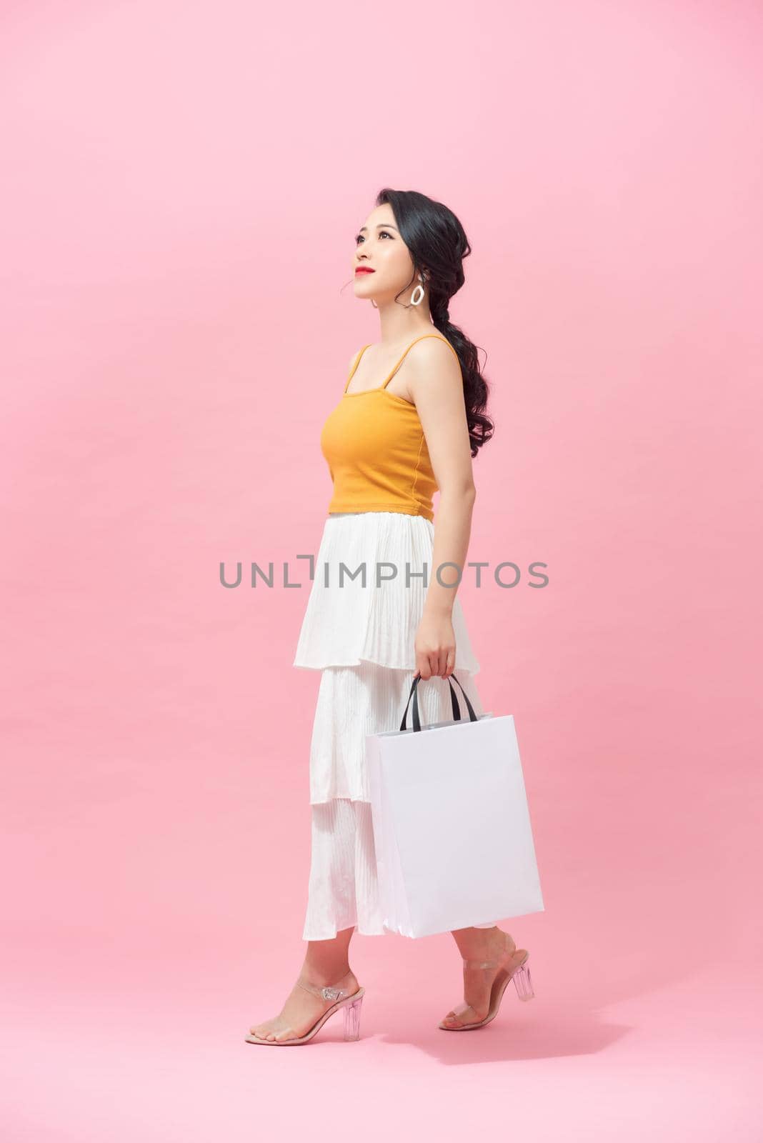 Charming young Asian woman happily shopping during sale season isolated on pink background. by makidotvn