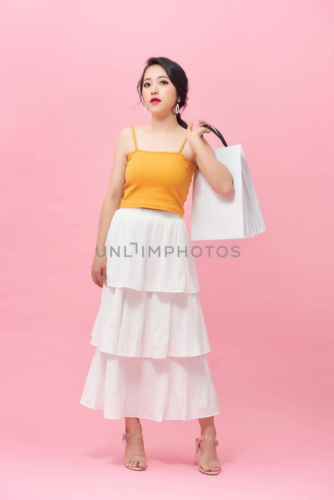 Full length portrait of smiling young woman with shopping bags over pink background.