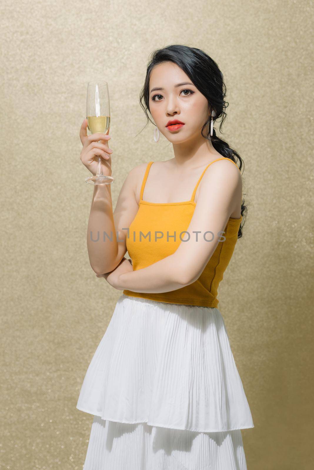 Attractive young Asian woman holding wine glass isolated over gold background.  by makidotvn