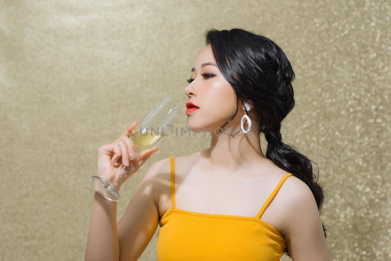 Portrait of cheerful young Asian woman drinking wine isolated over gold background. by makidotvn
