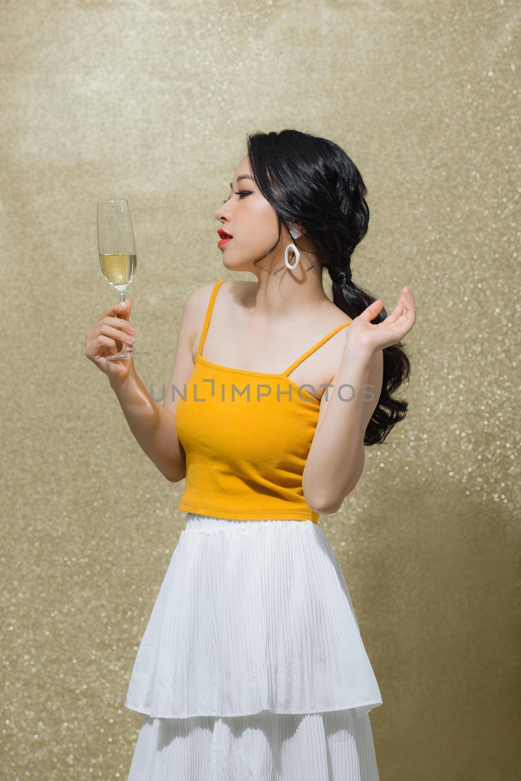 Beautiful young Asian woman raising wine glass over gold background. Party concept. by makidotvn