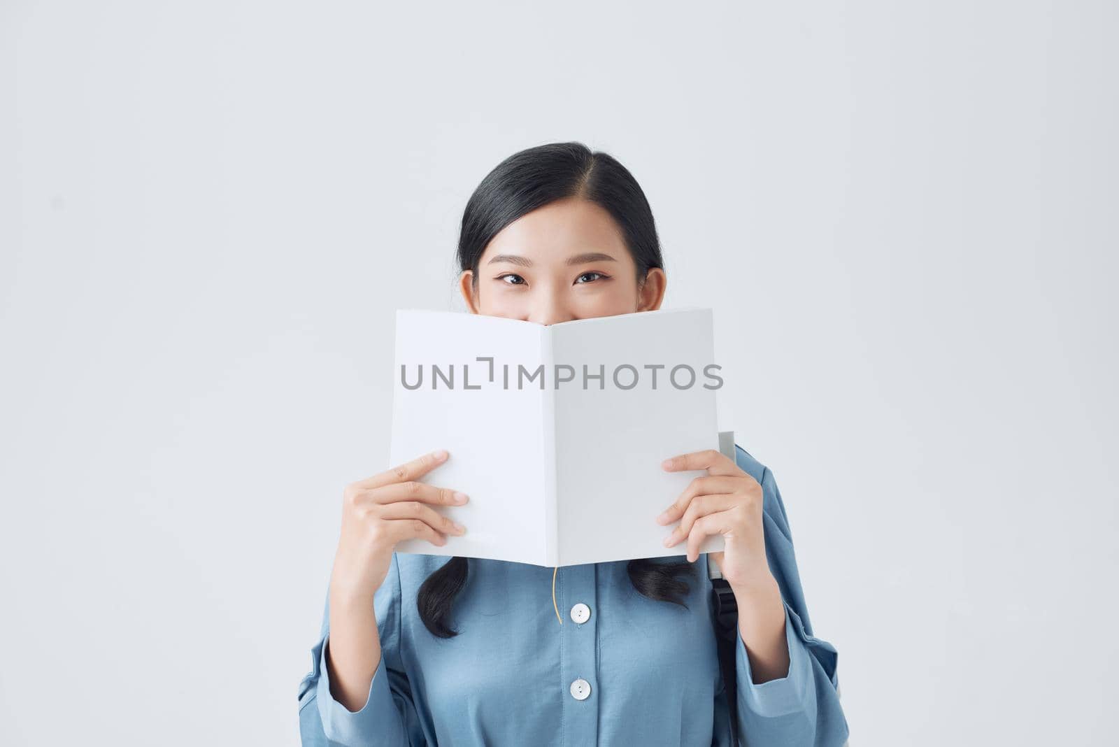 Happy pensive girl holding white notebook, covering half of face, looking attentively at camera,