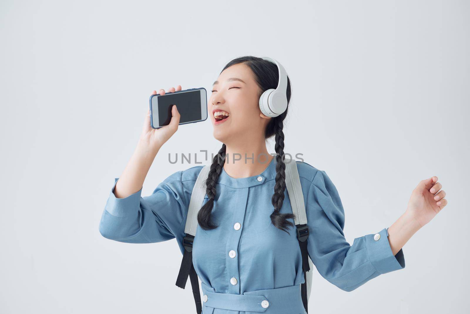 Excited asian woman posing isolated over white background listening music with headphones dancing singing.