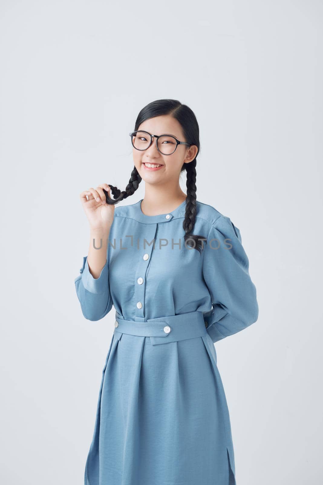 Young beautiful lady holding two hair braids in hands happily looking in camera over white background