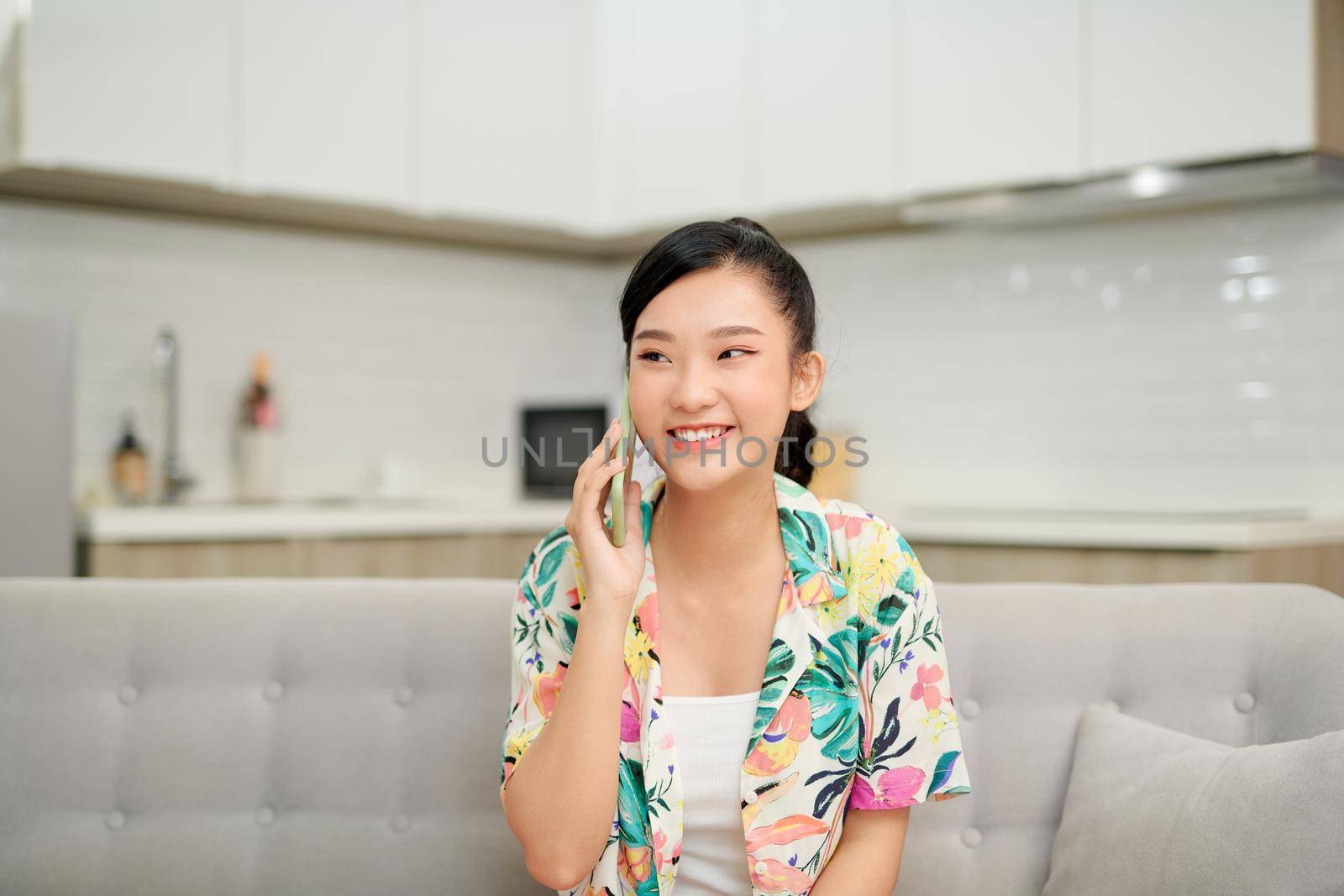 Pleasant talk with friend. Attractive smiling young redhead woman talking on cell phone while sitting on the beige sofa at home