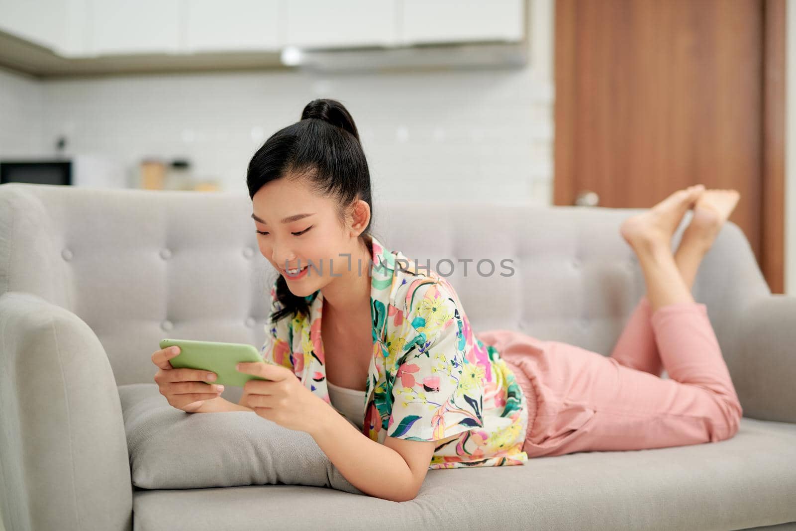 Smiling young asian woman using mobile phone app playing game, relax on sofa.
