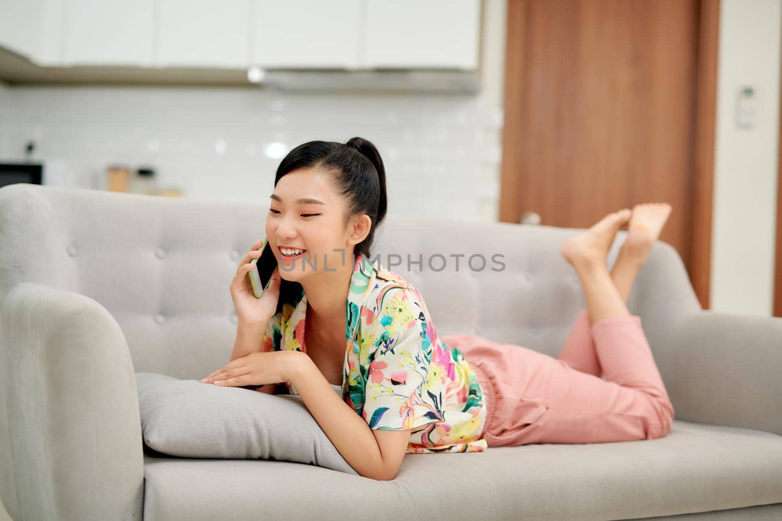 Happy young woman talking mobile phone while relaxing on couch