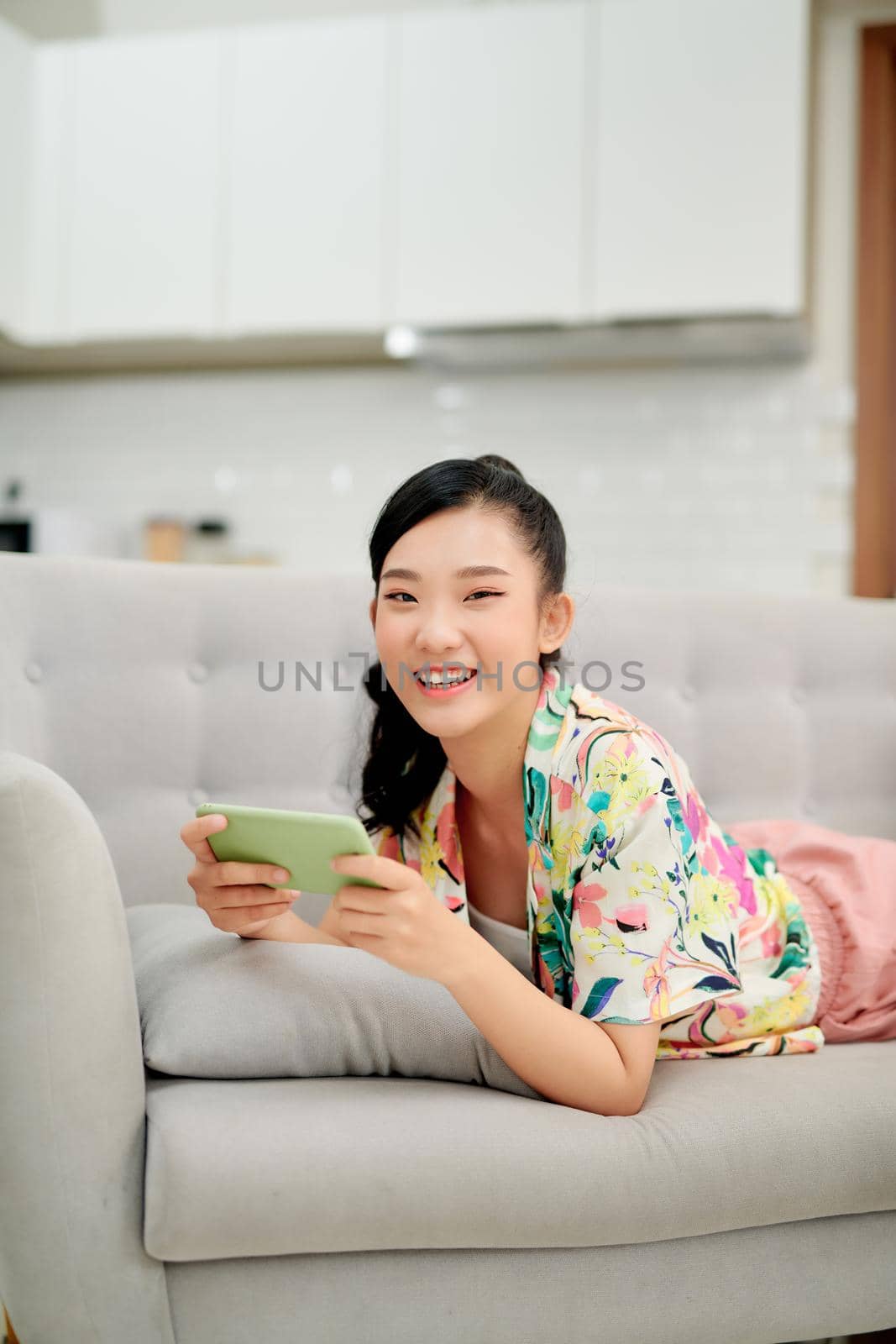 Woman lying on sofa and play mobile game happily at home