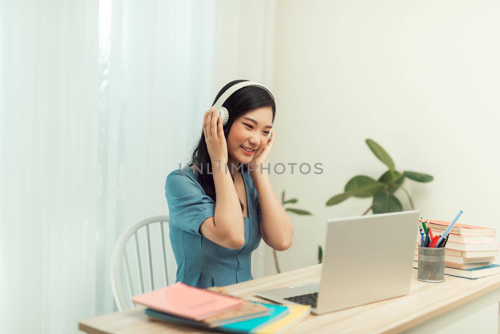 Dedicated female freelancer in glasses and wireless headphones smiling at camera while sitting at laptop with mug  by makidotvn