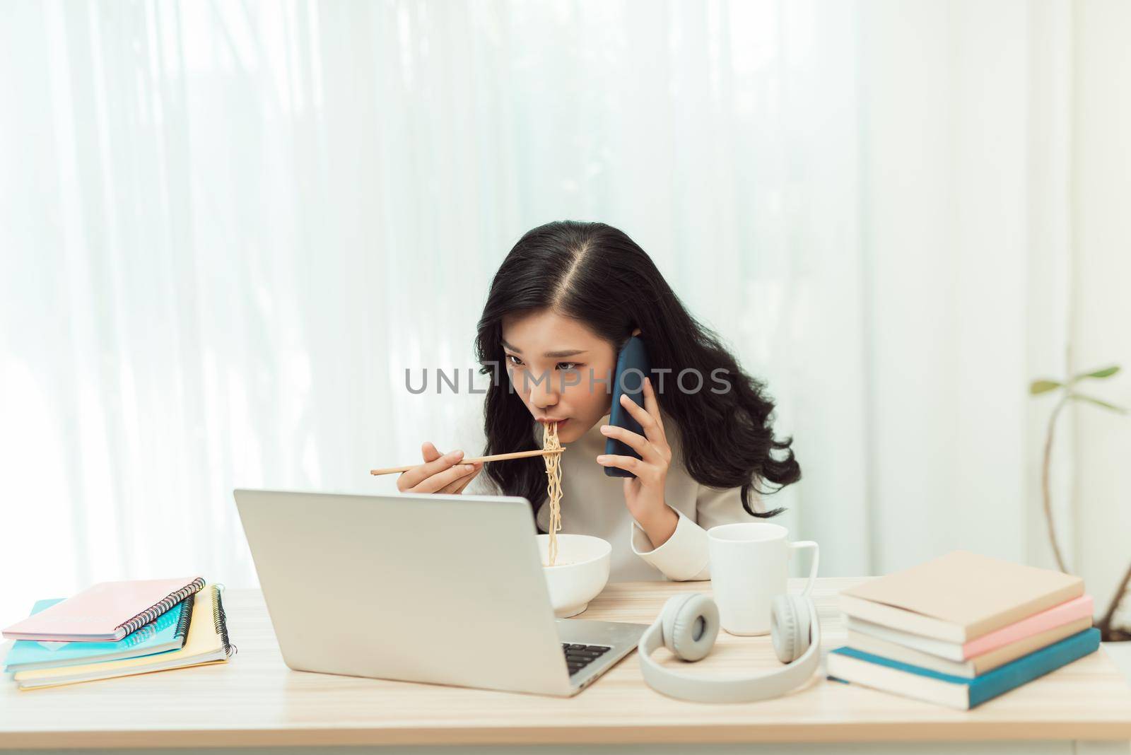 Confident smiling attractive young asian woman entrepreneur having lunch break while sitting at the office desk and using mobile phone by makidotvn