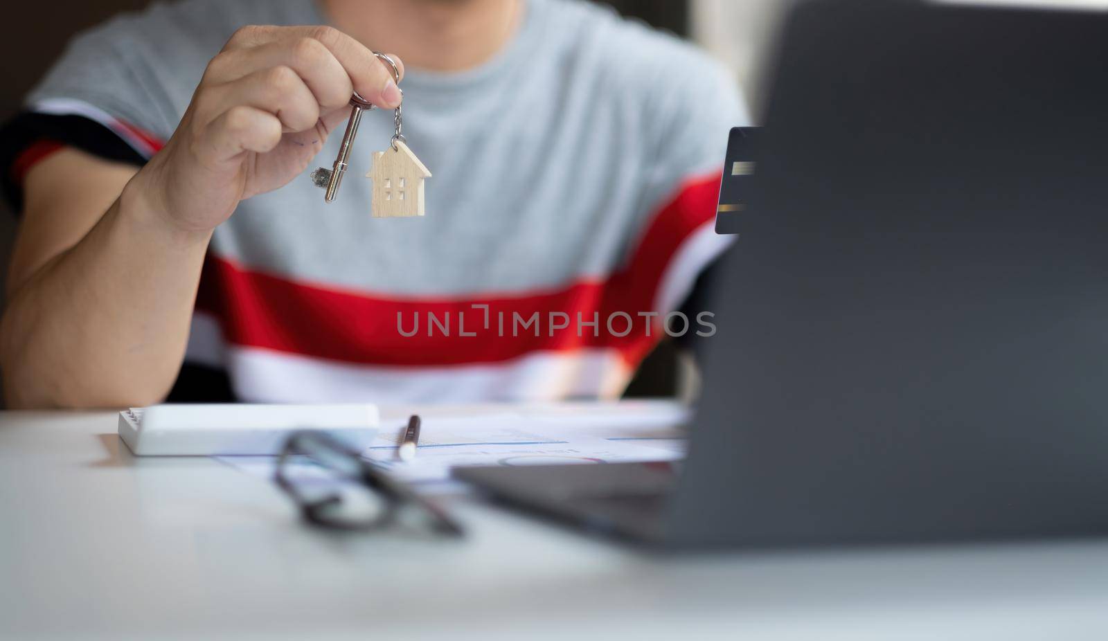 Real estate agent holding house key on table with house designs document,calculator,model house.Concept for real estate. by nateemee