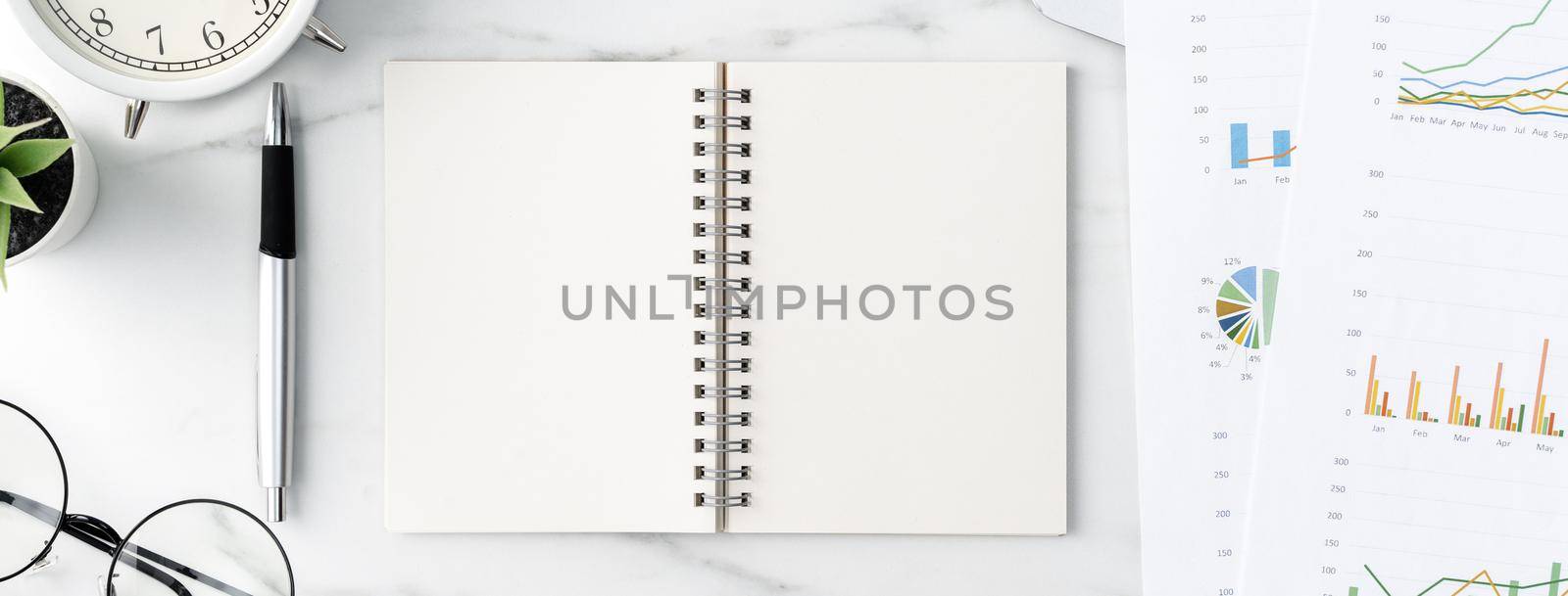 Top view of office table desk work concept with blank notebook, report, alarm clock on marble white background, concept of timing management and schedule planning.