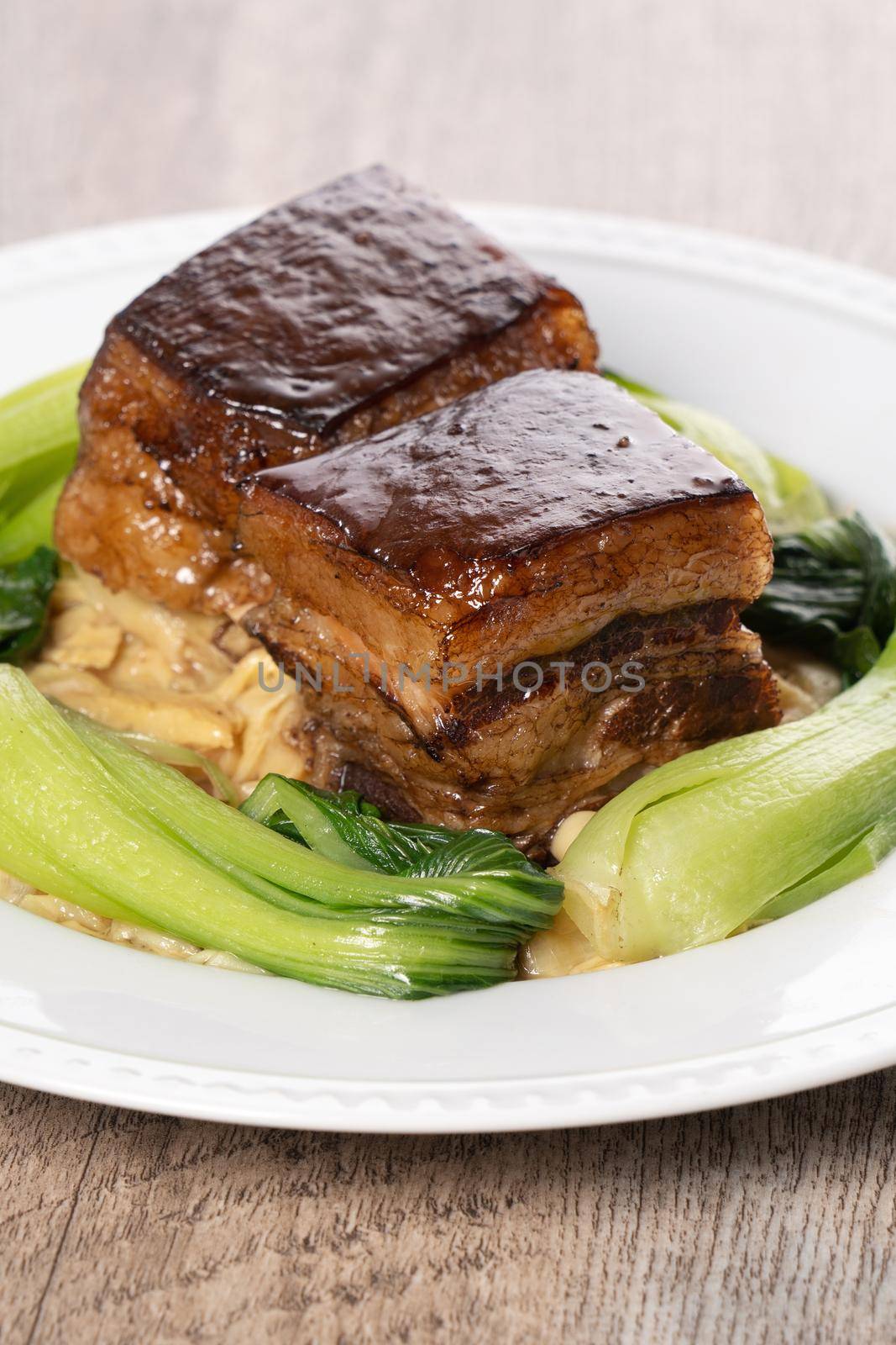 Dong Po Rou (Dongpo pork meat) in a beautiful white plate with green vegetable, traditional festive food for Chinese new year cuisine meal, close up.