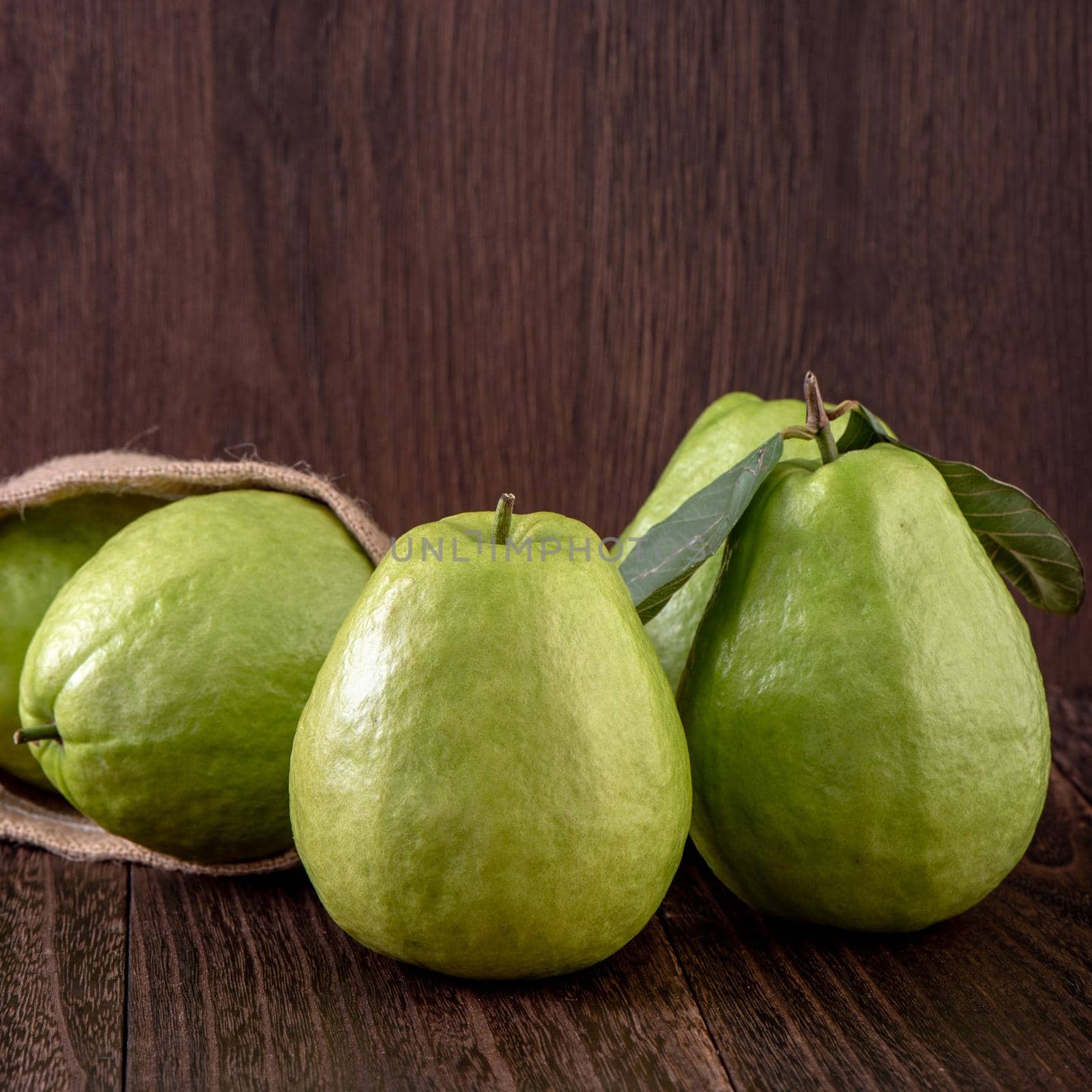 Close up of delicious beautiful guava set with fresh green leaves isolated on dark wooden table background.