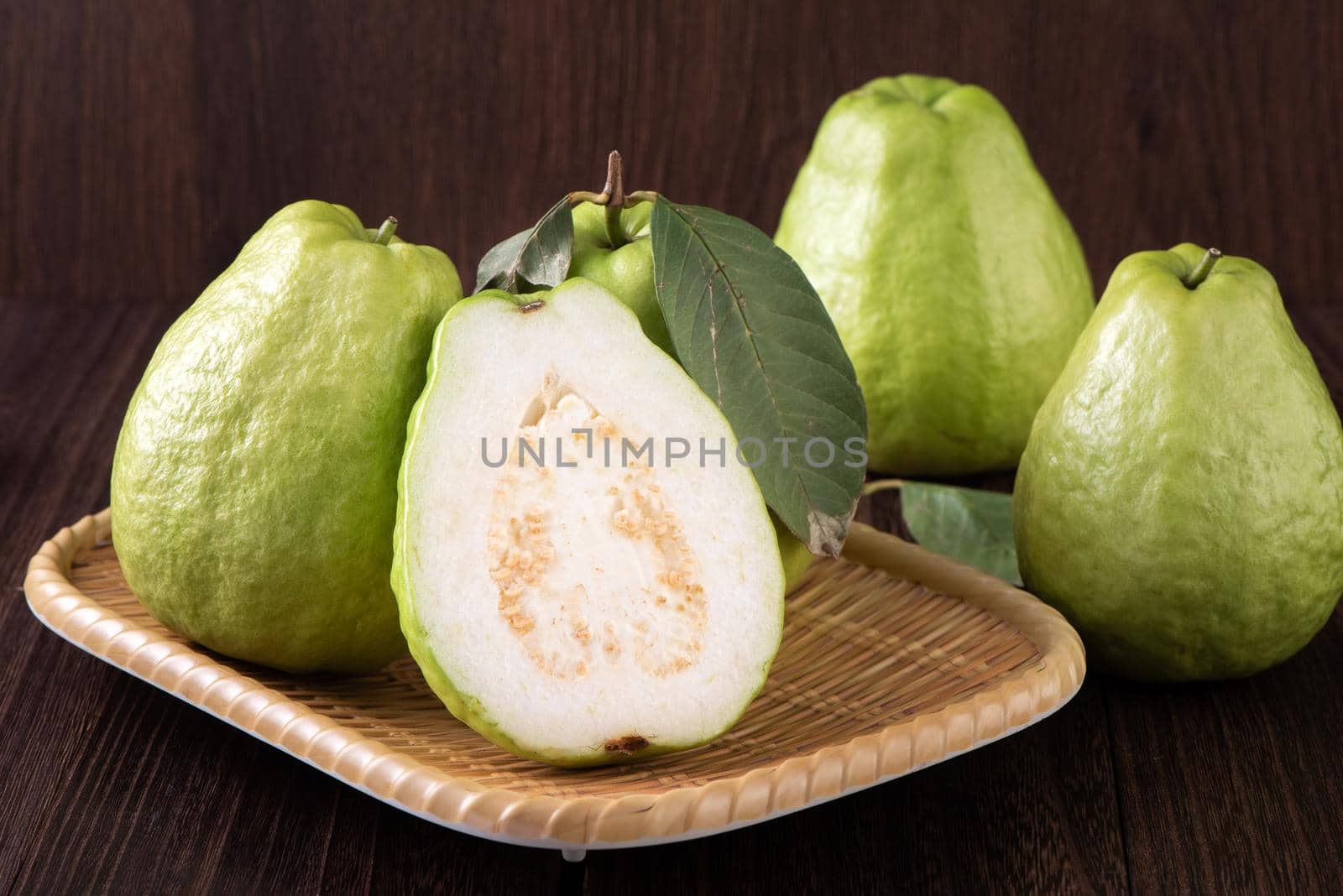 Close up of delicious beautiful guava set with fresh green leaves isolated on dark wooden table background.