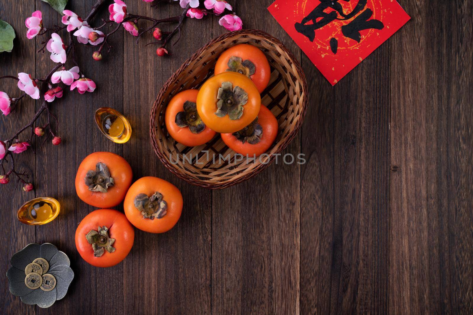 Top view of fresh sweet persimmons kaki with leaves on wooden table background for Chinese lunar new year fruit design concept, the word means blessing is coming.