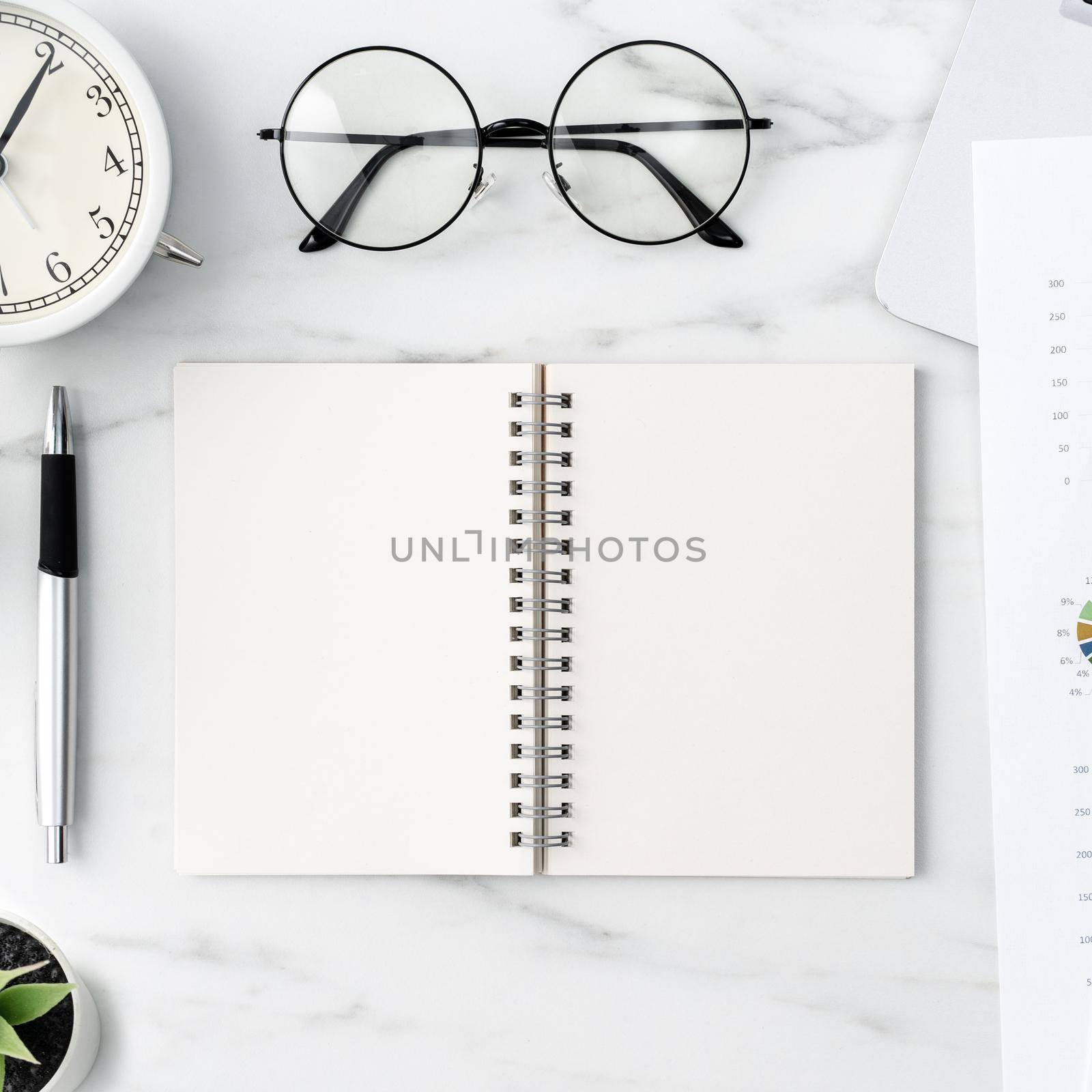 Top view of office table desk work concept with blank notebook, report, alarm clock on marble white background, concept of timing management and schedule planning.