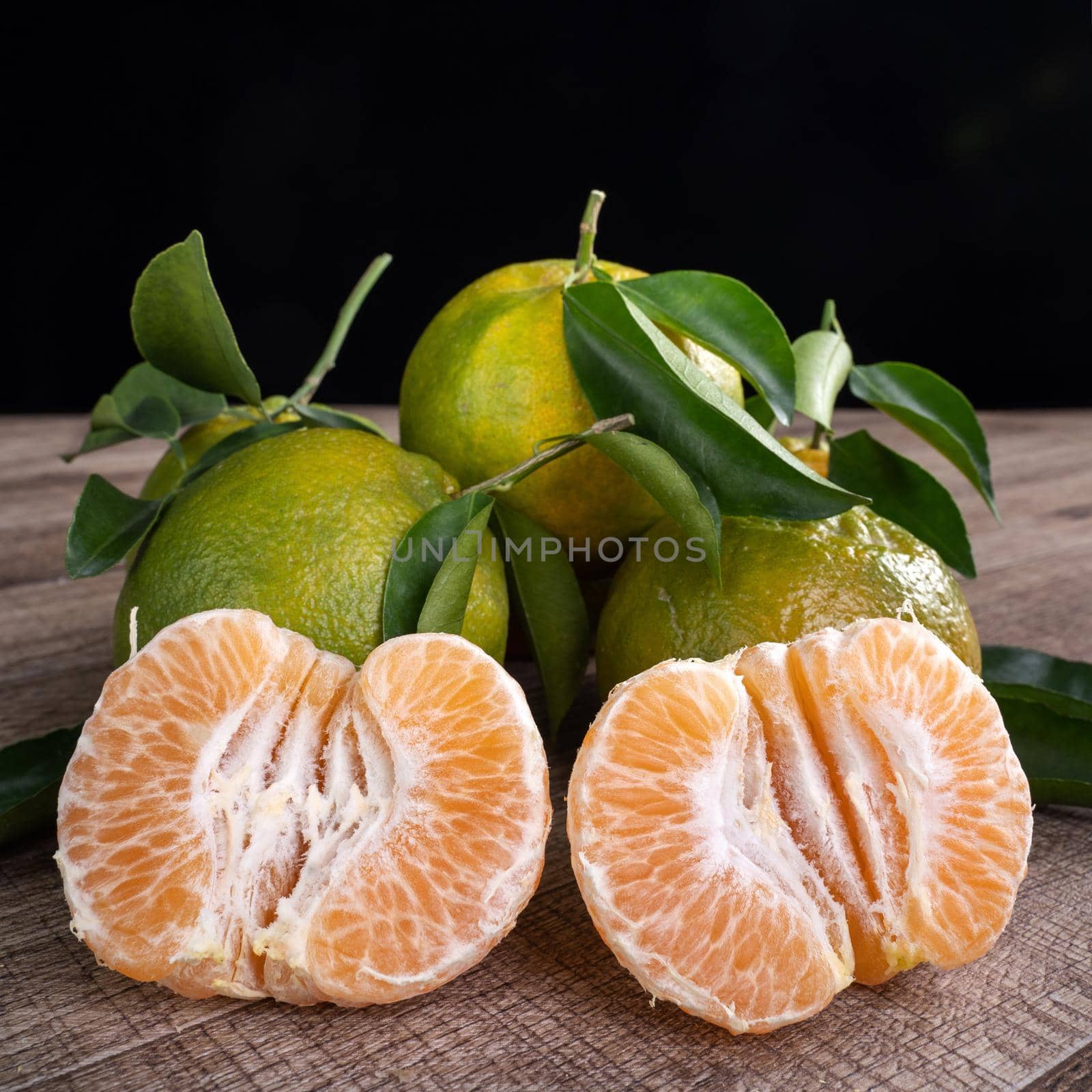 Fresh green tangerine mandarin orange with fresh leaves on dark wooden table background harvest concept.