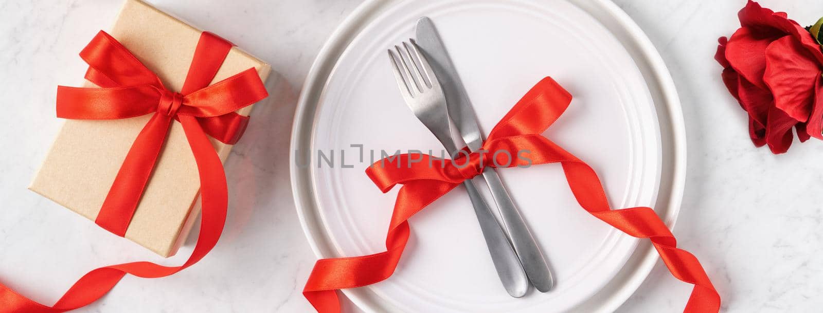 Empty white plate with tableware, ribbon, gift and roses for Valentine's Day special holiday dating meal concept.