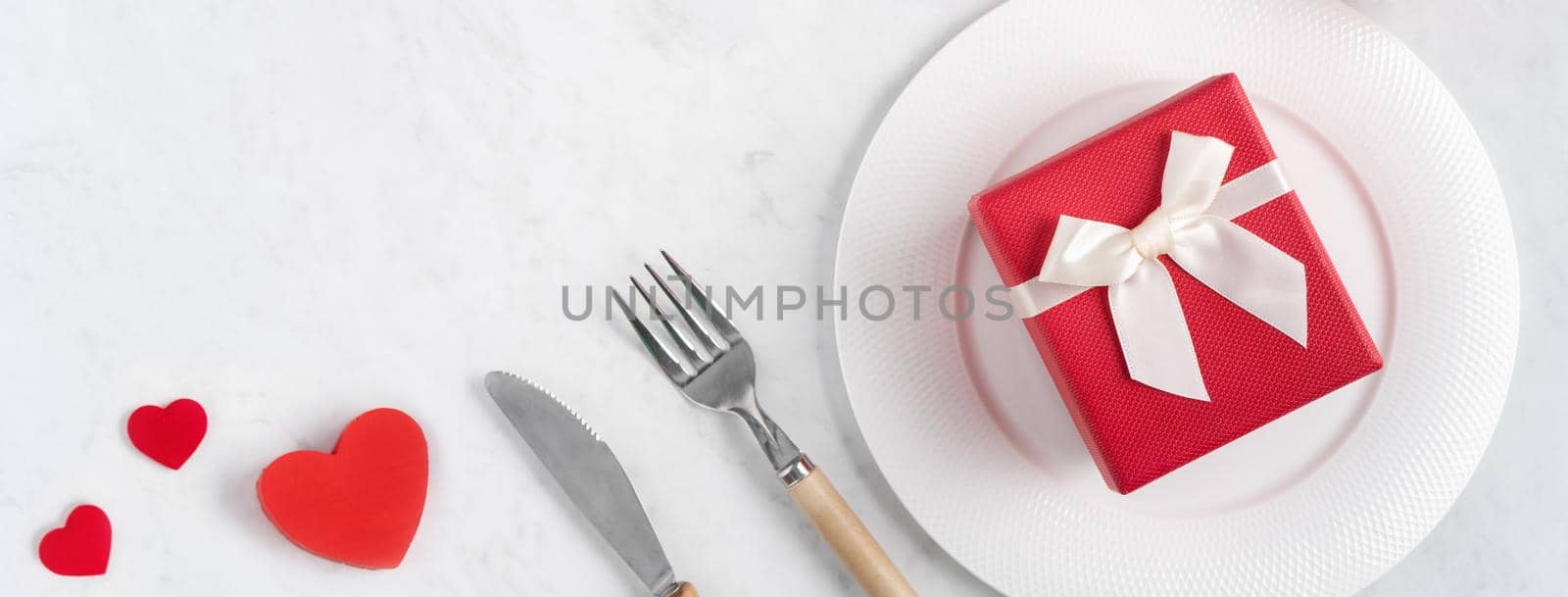 Empty white plate with tableware, ribbon, gift and roses for Valentine's Day special holiday dating meal concept.