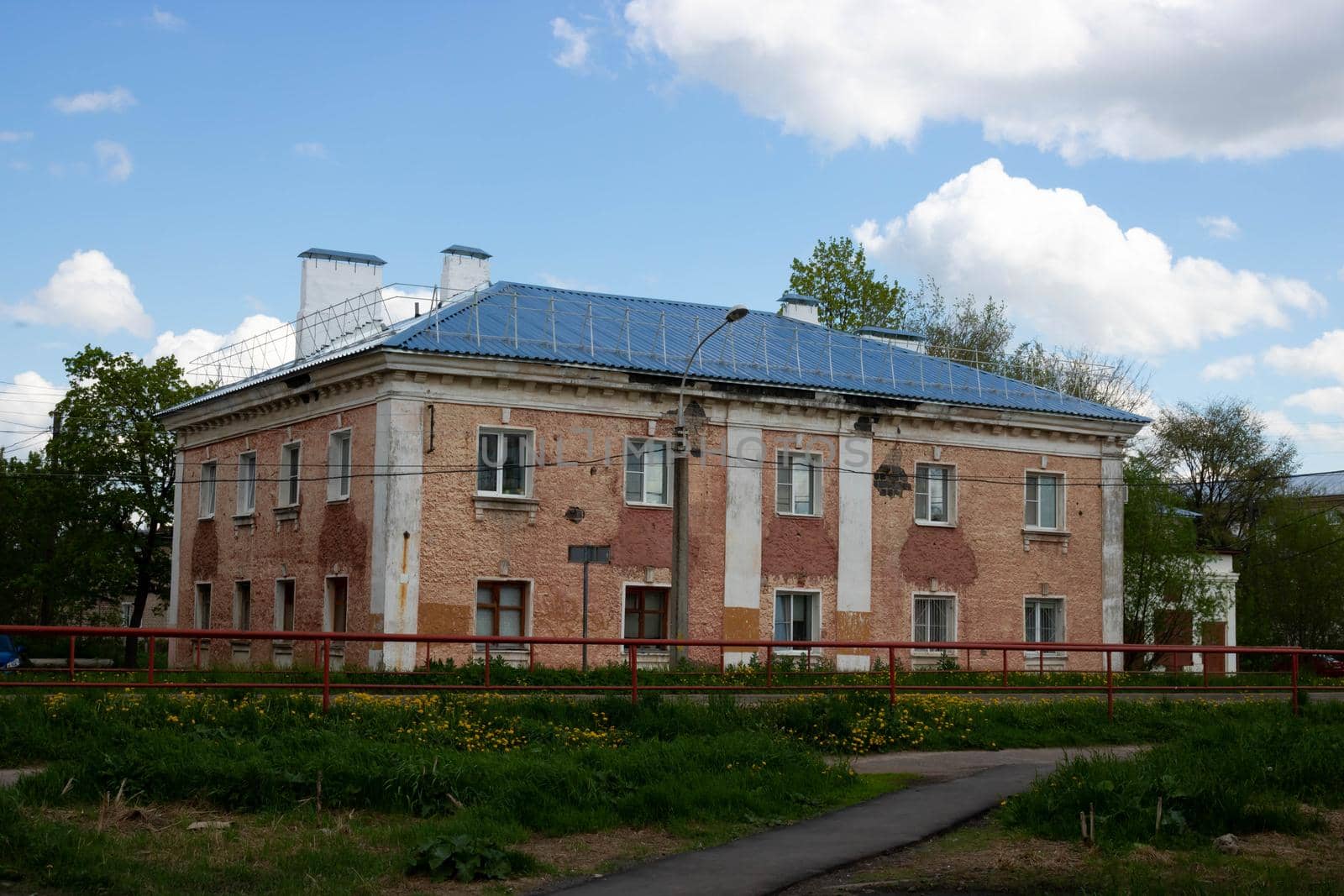Two-story apartment building old red house with stucco walls against a blue sky with clouds.