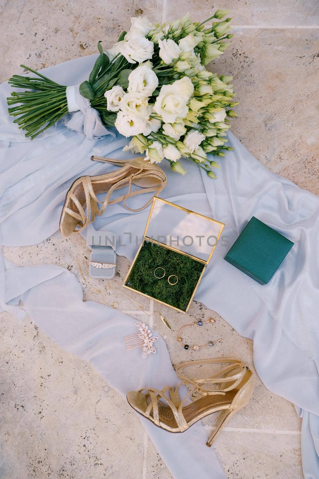 Two wedding rings and bridal accessories on a white fabric with a bouquet of flowers and sandals with heels. High quality photo