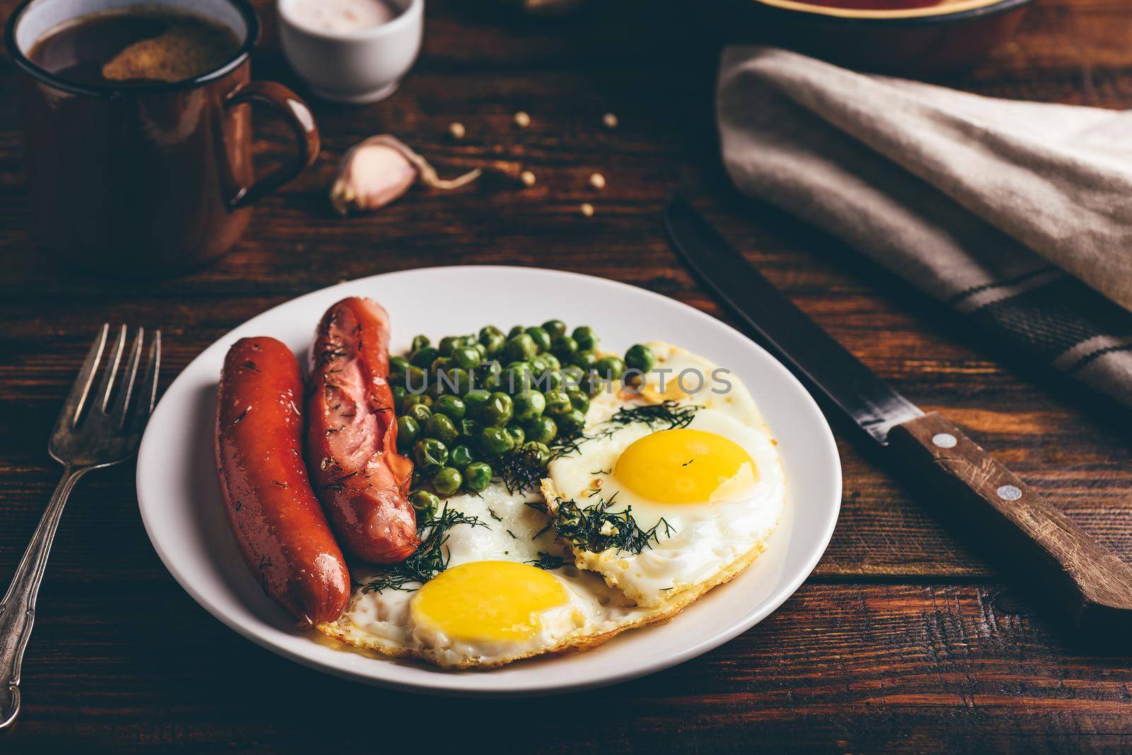 Breakfast with fried eggs, sausages and green peas on white plate