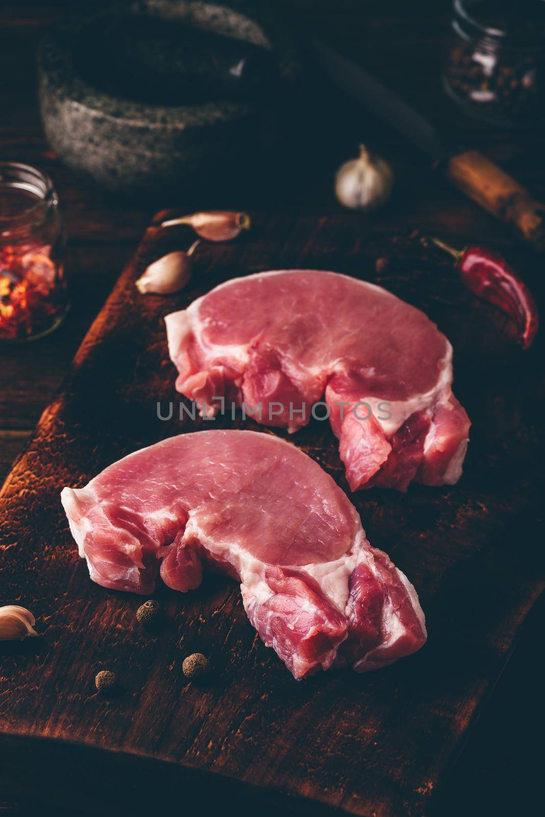 Two raw pork loin steaks on chopping board