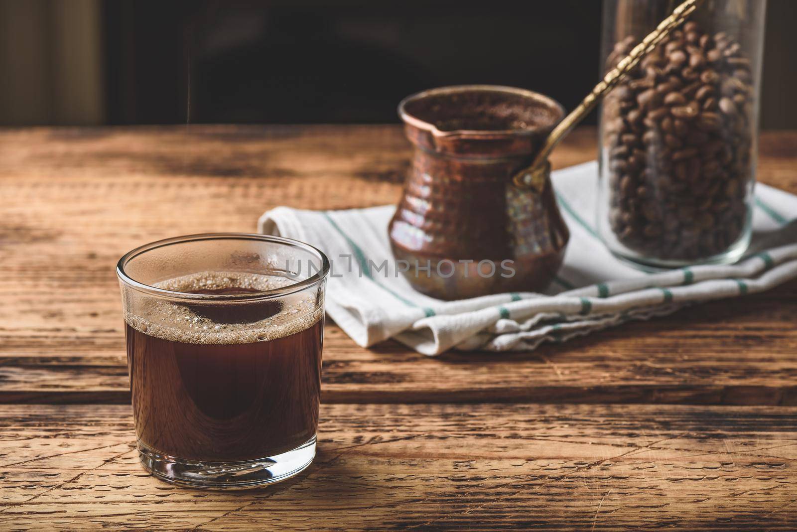 Freshly brewed turkish coffee in drinking glass. Cezve and jar of roasted coffee beans.