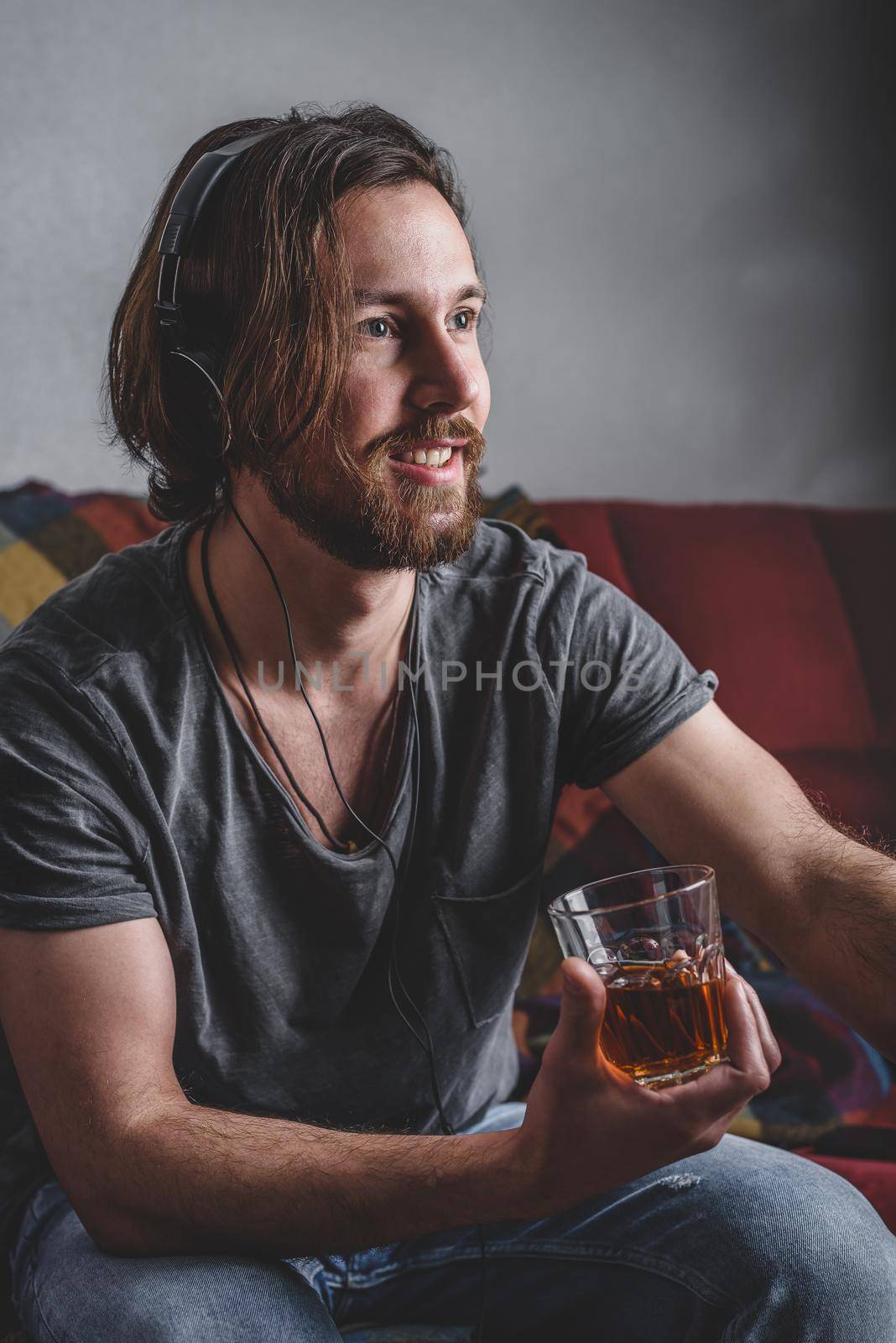 Bearded man listening to music with headphones and holding glass with tea in his hand