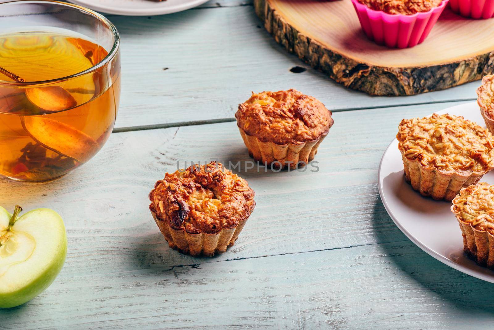 Healthy Breakfast. Cooked oatmeal muffins with apple and cup of green tea over light wooden background.