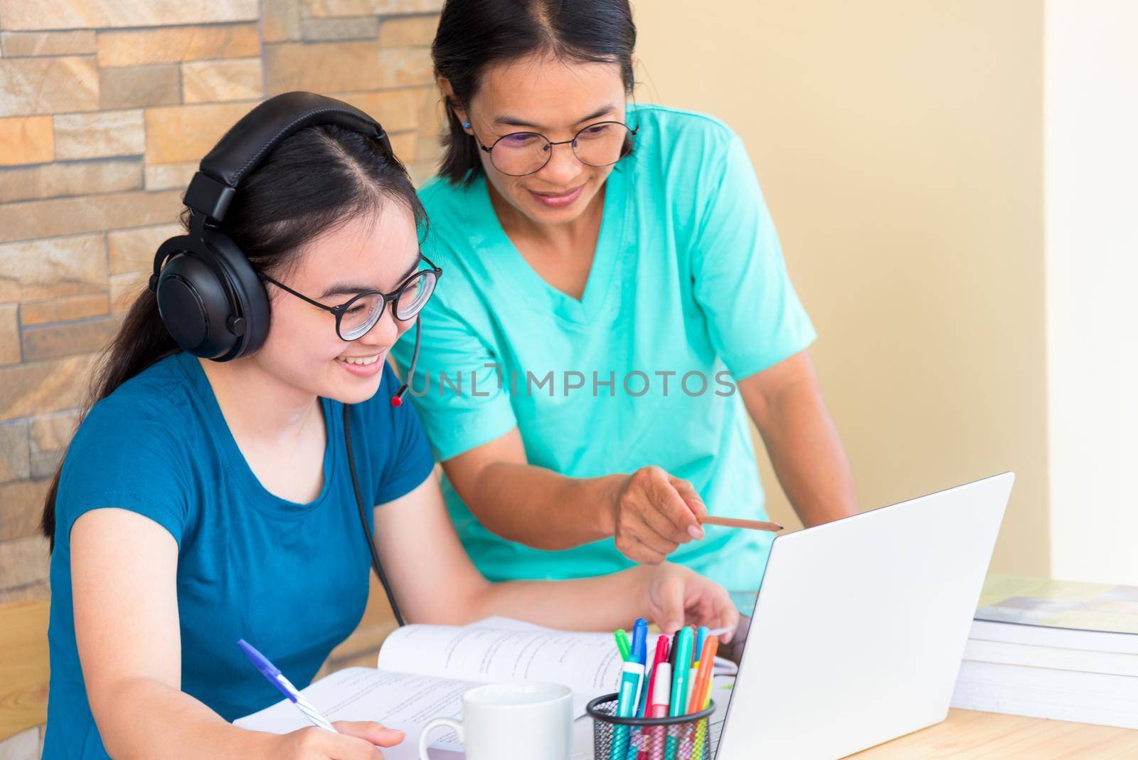 Happy two Asian woman mother is a teacher advice instruction to her daughter teenage girl student online study from school using a laptop computer education from university class learning from home