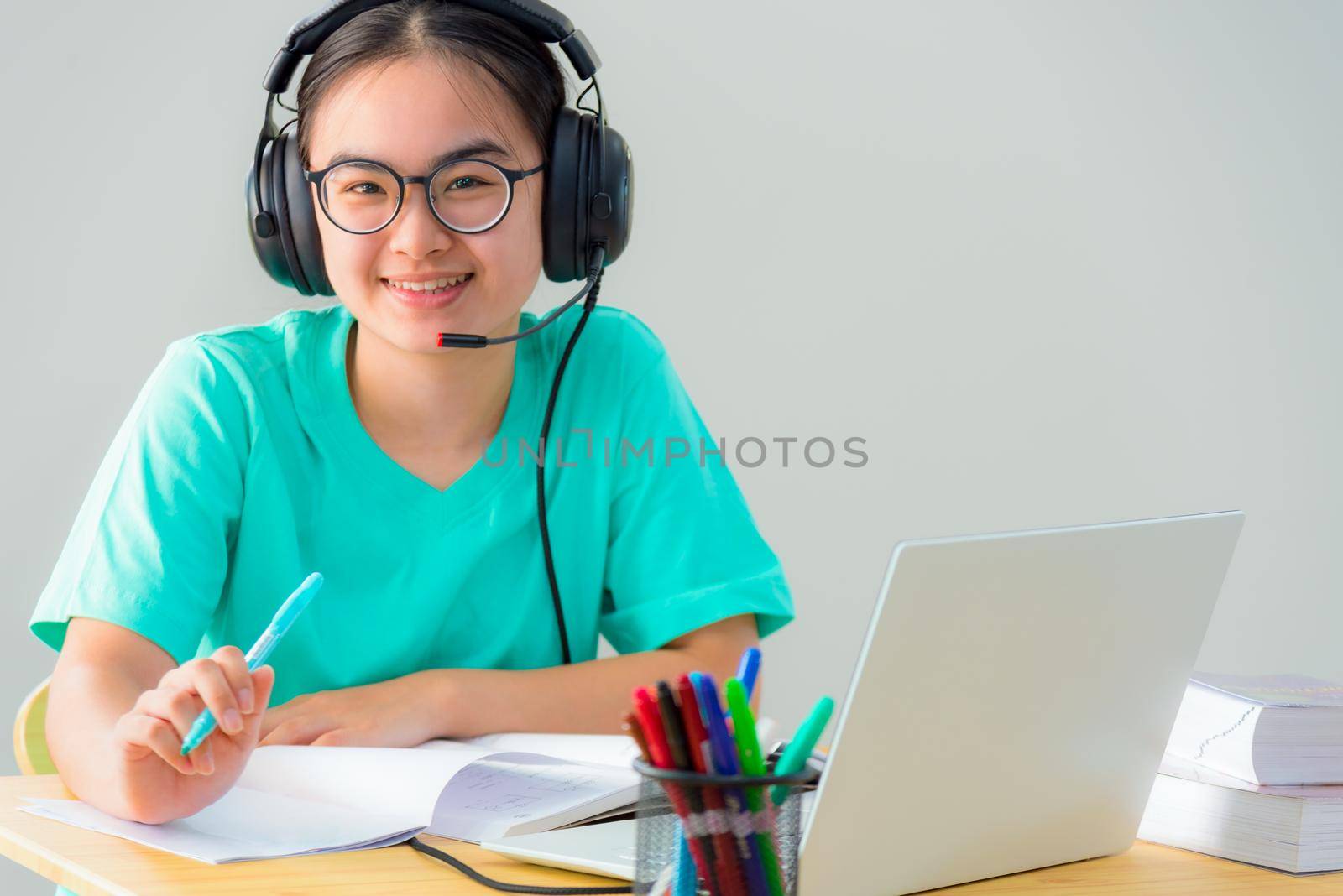 Portrait Asian young woman student glasses headphones sitting happy study smile looking up online class college learning internet education, Teenage girl work distance on a laptop computer from home