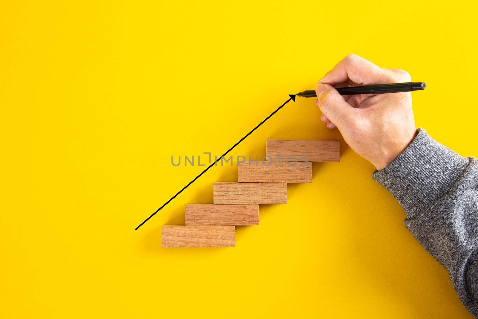 Man hand drawing an upward pointing arrow on top of growing graph made of wooden block. by tehcheesiong