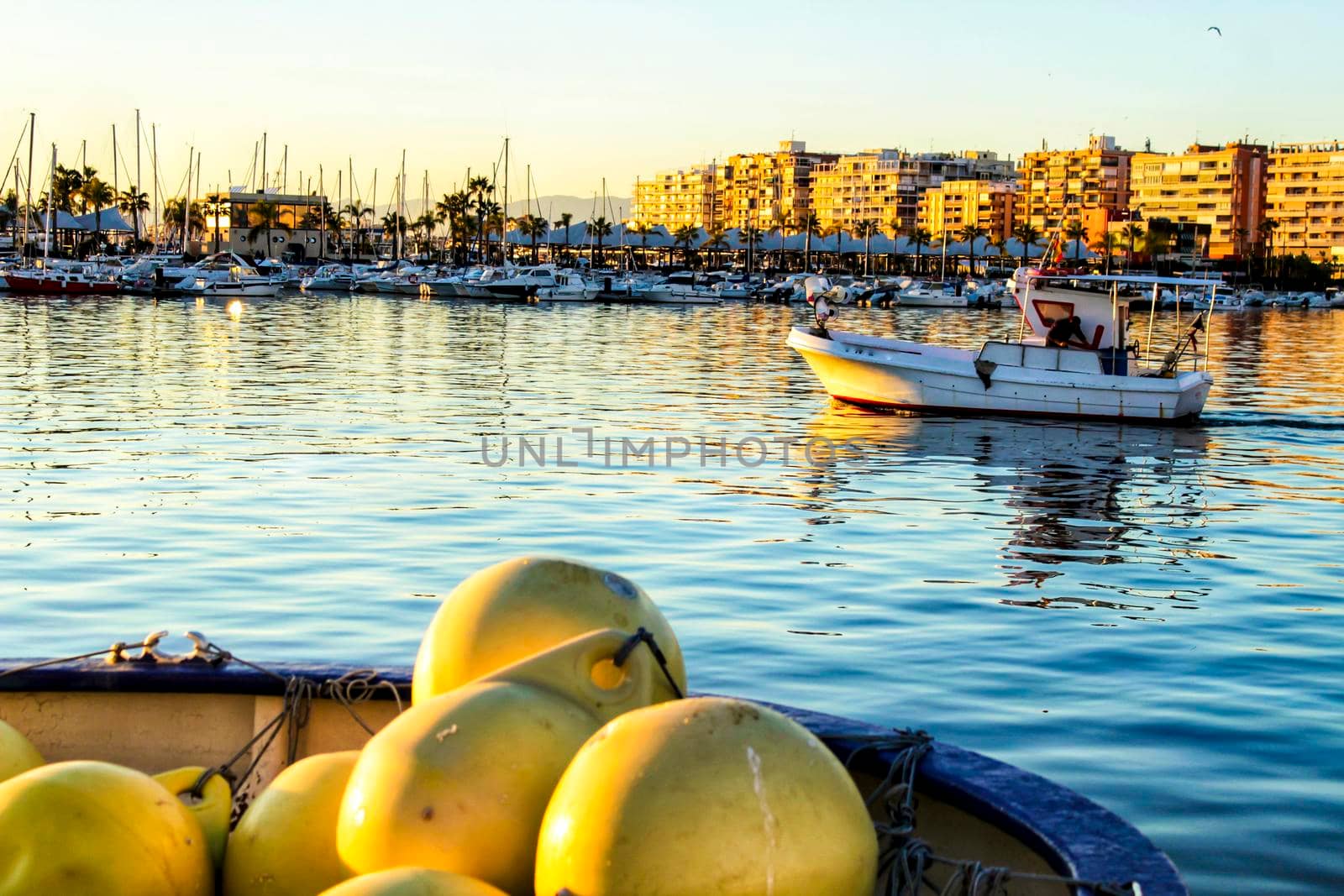 Boat going out to fish in the port. Yellow buoys in the foreground