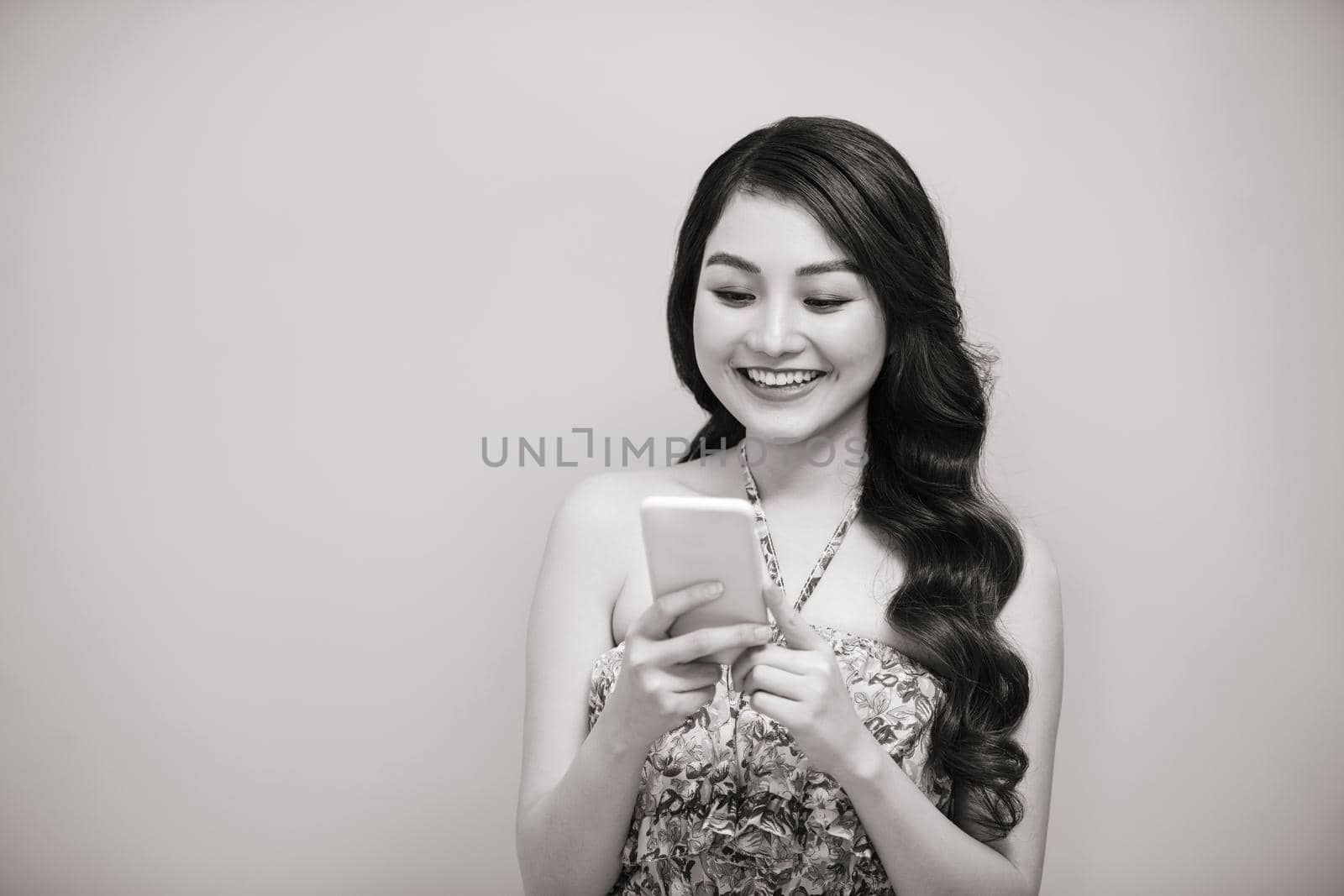 Portrait of a smiling casual woman holding smartphone over white background. Black-white photo.