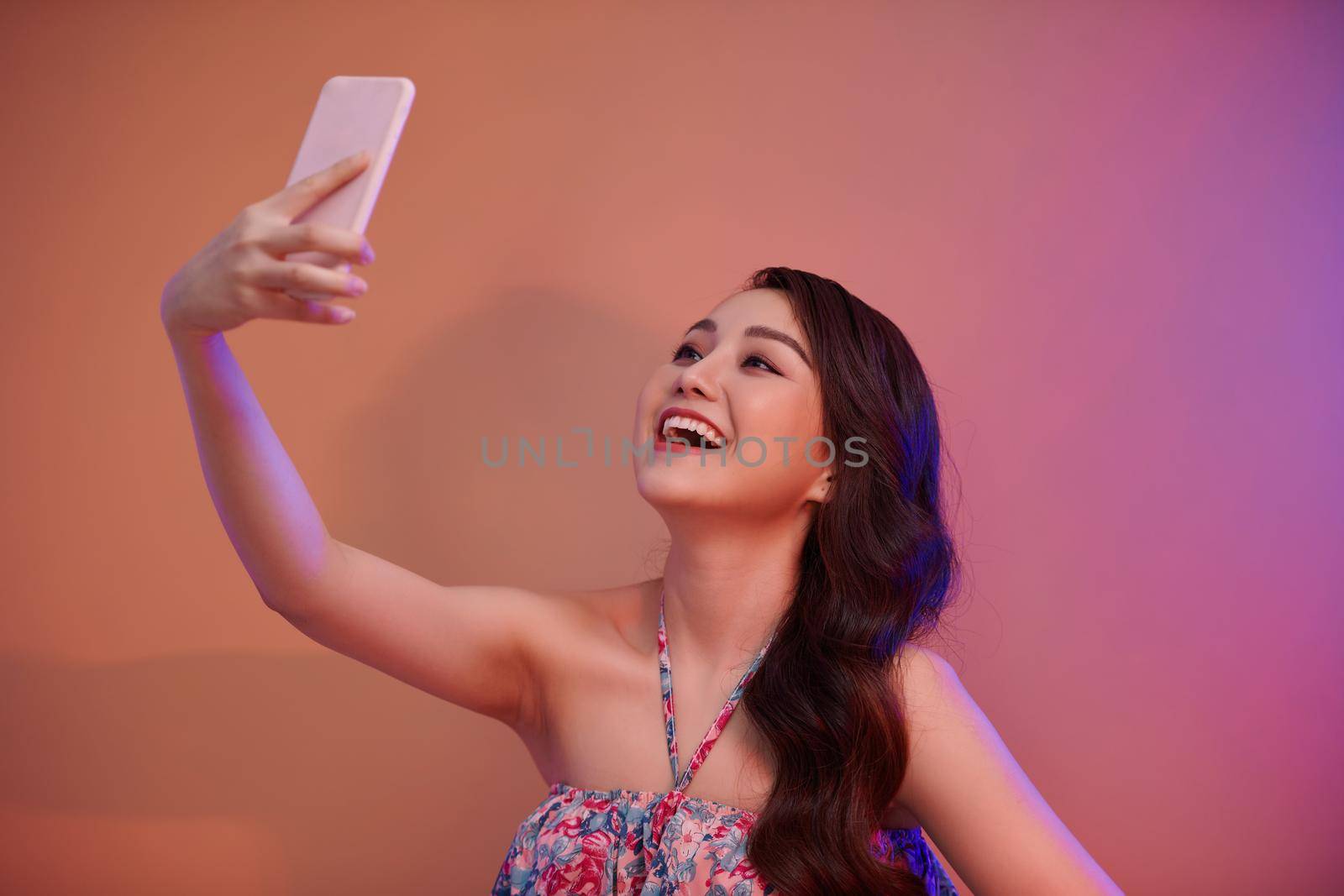 a smiling woman making selfie photo on smartphone  in neon light in the studio