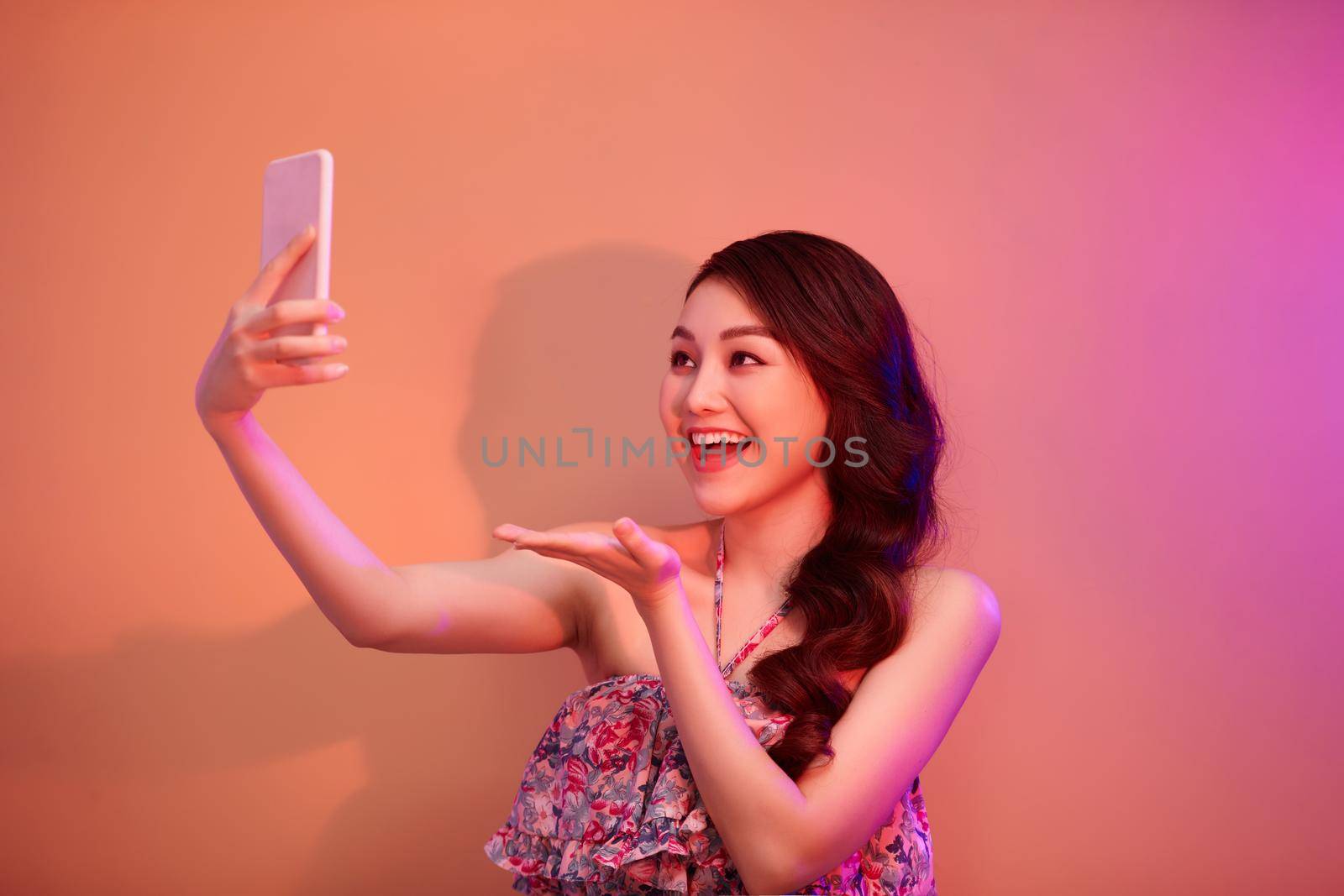 a smiling woman making selfie photo on smartphone  in neon light in the studio by makidotvn