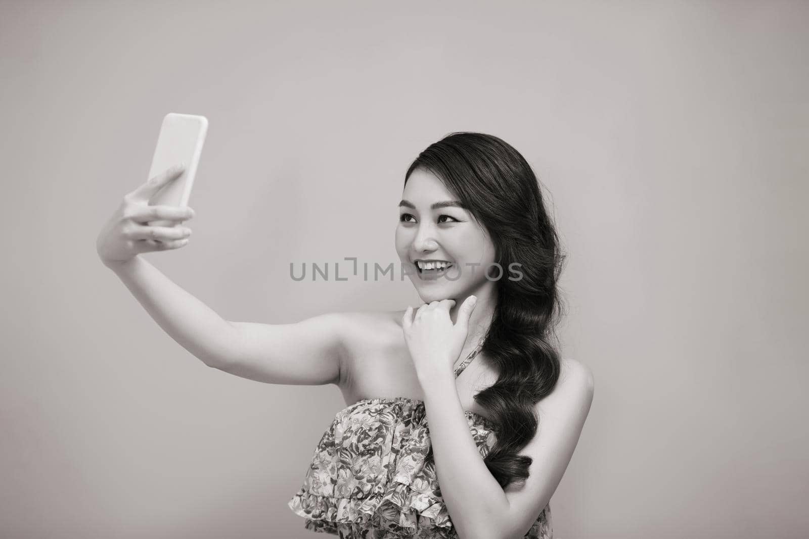 Young woman taking selfie photo on smartphone looking camera laughing happy. Black and white photo by makidotvn
