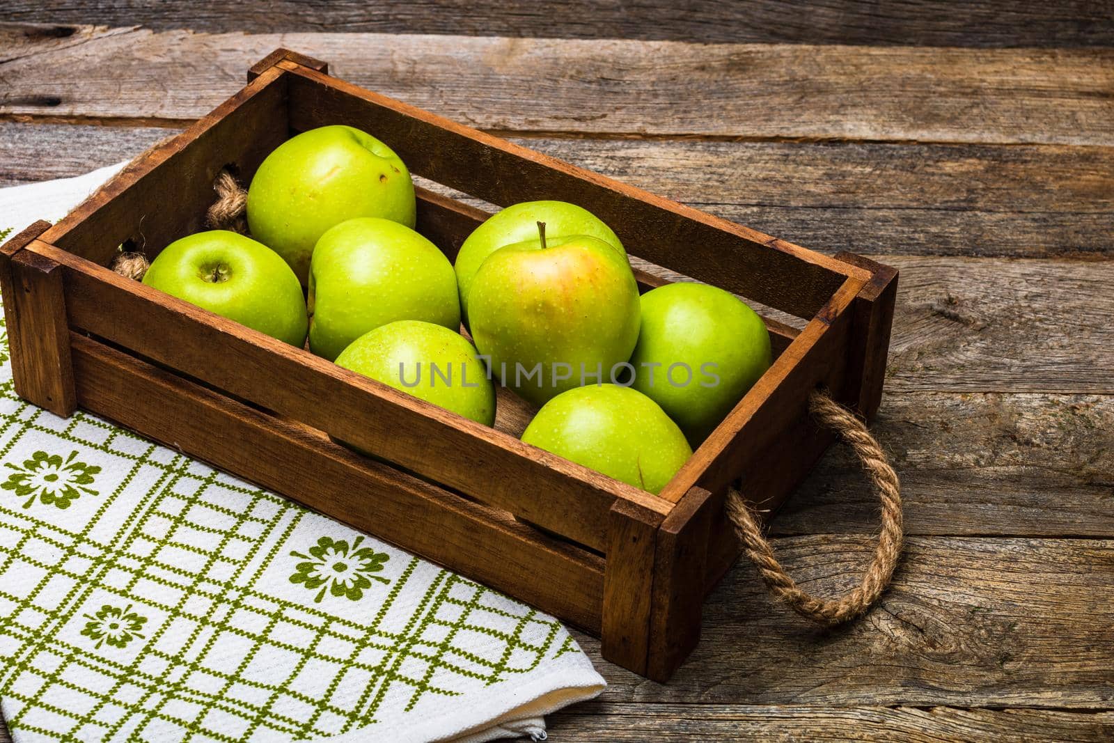 Wooden crate with ripe green apples on wooden table.