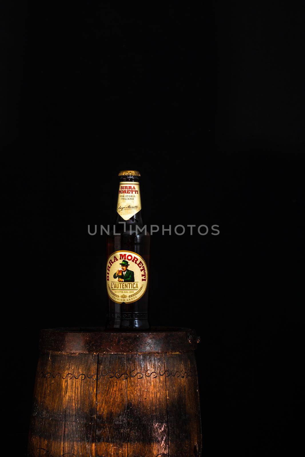 Bottle of Birra Moretti beer on wooden barrel with dark background. Illustrative editorial photo Bucharest, Romania, 2021 by vladispas