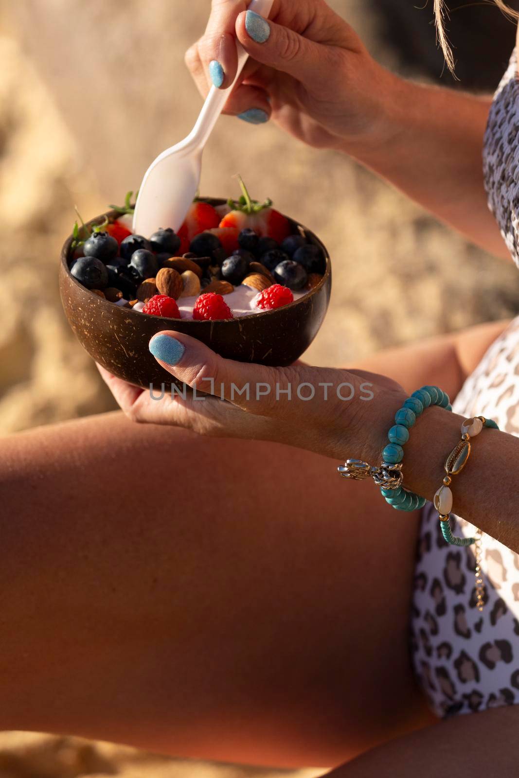 Woman eating a healthy breakfast from a coconut bowl on  sunny beach in summer