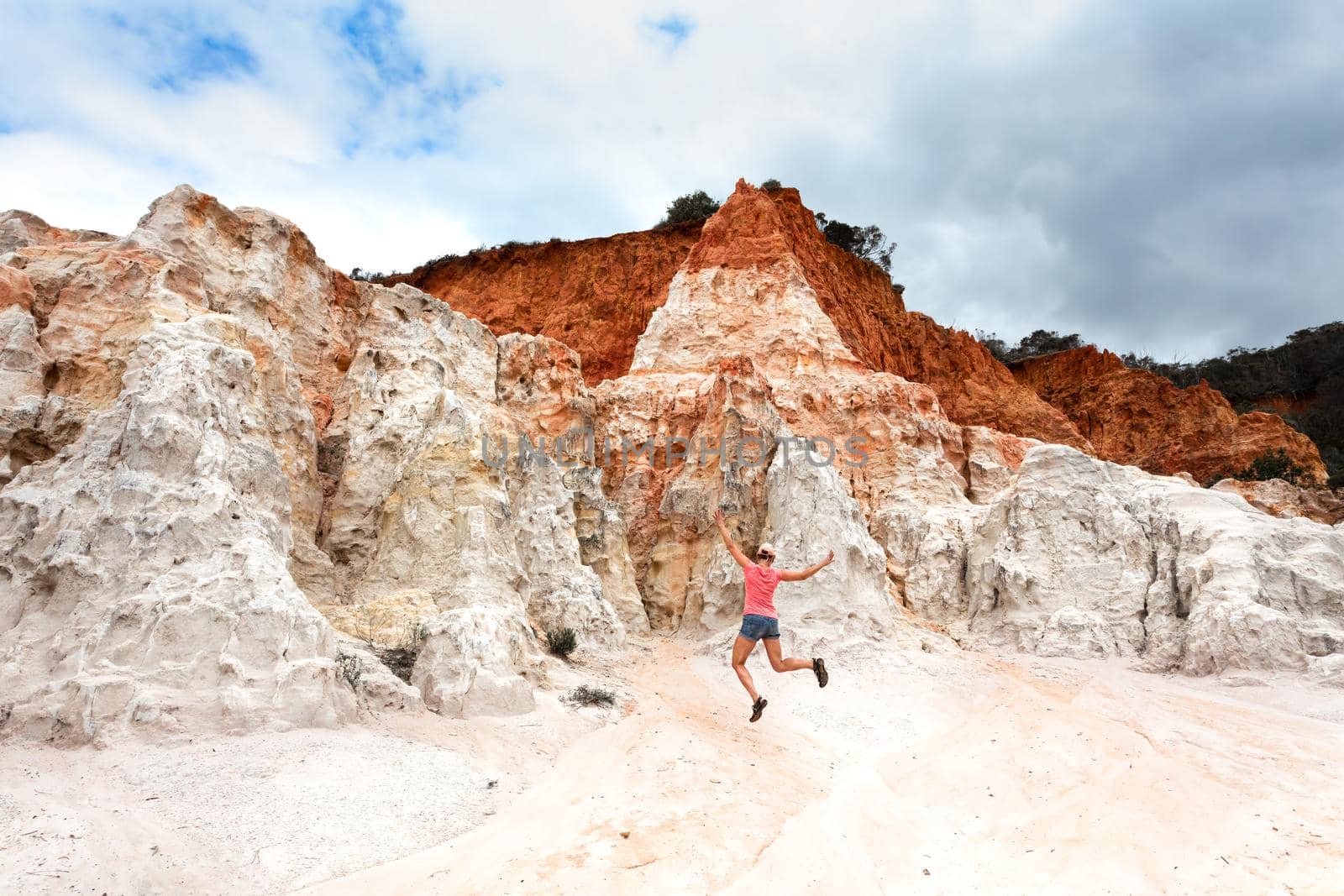 Female jumping among the amazing awe inspiring red white and orange rock formations at Ben Boyd  Eden