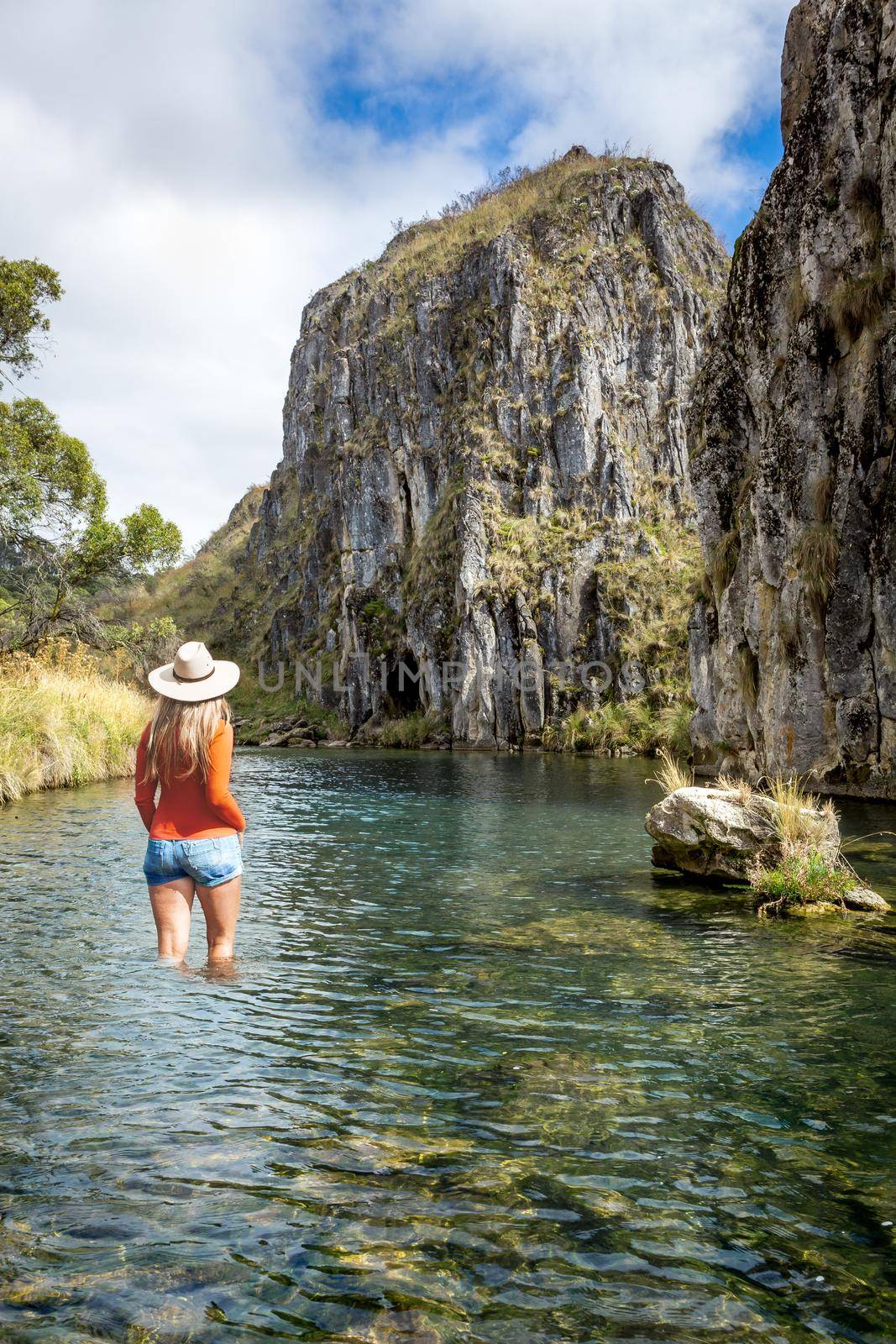 A woman traveller in high country Australia stands in a shallow mountain stream with views to mountain caves eroded by the water