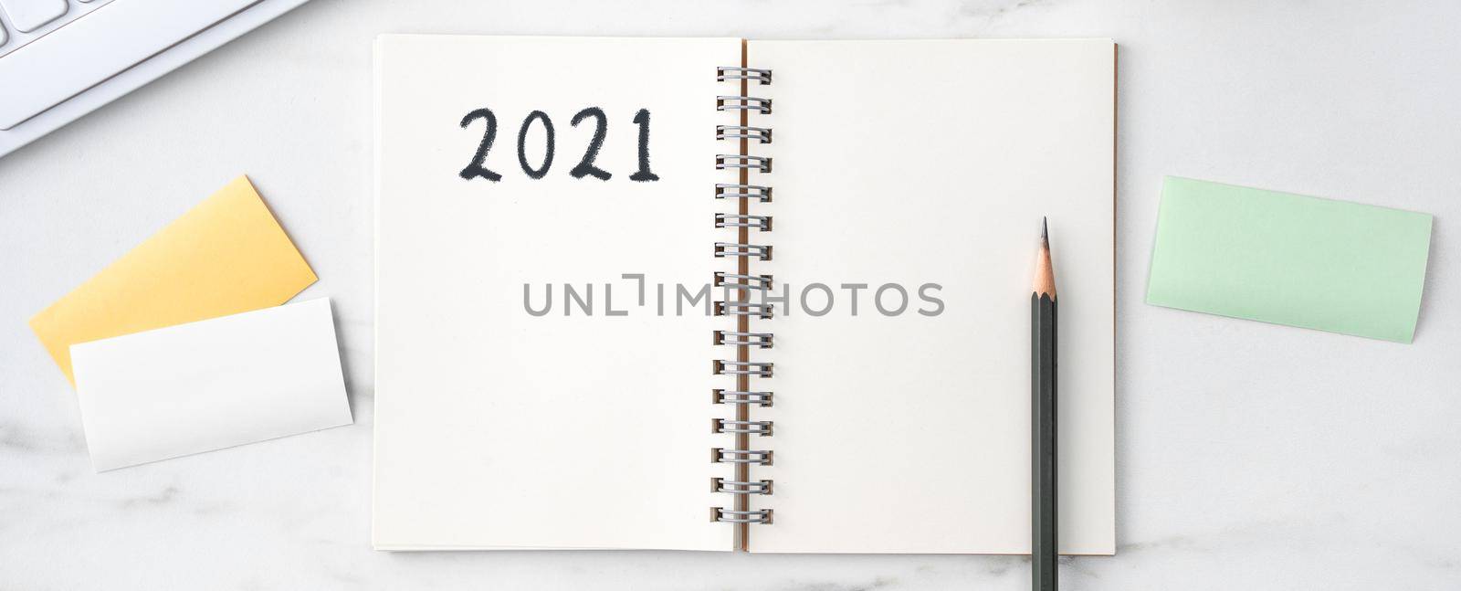Top view of office table desk 2021 Goal work concept with keyboard, notebook, pencil, eyeglasses and coffee on bright marble white background.