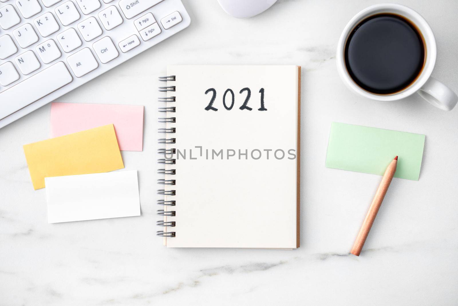 Top view of office table desk 2021 Goal work concept with keyboard, notebook, pencil, eyeglasses and coffee on bright marble white background.
