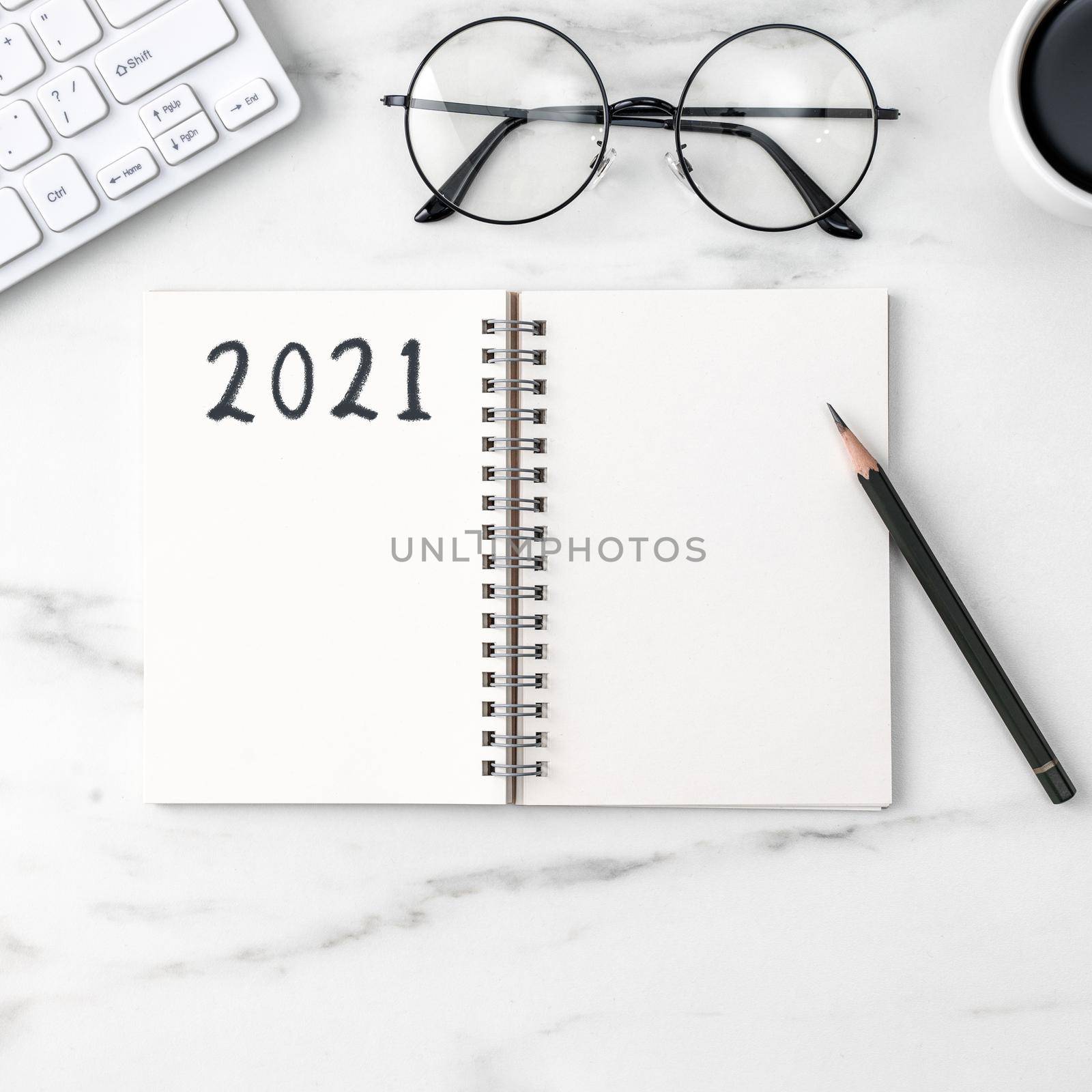Top view of office table desk 2021 Goal work concept with keyboard, notebook, pencil, eyeglasses and coffee on bright marble white background.