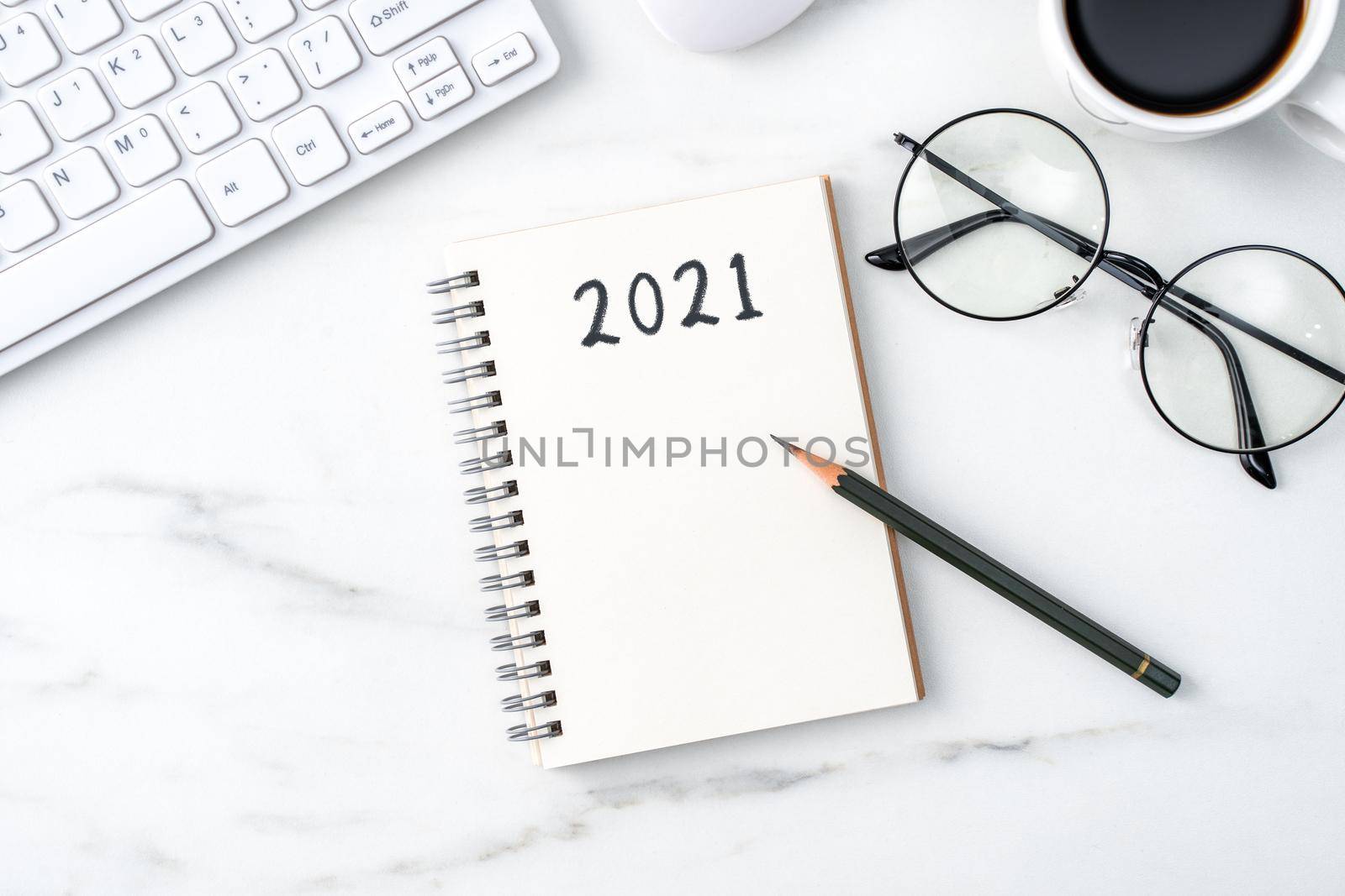 Top view of office table desk 2021 Goal work concept with keyboard, notebook, pencil, eyeglasses and coffee on bright marble white background.